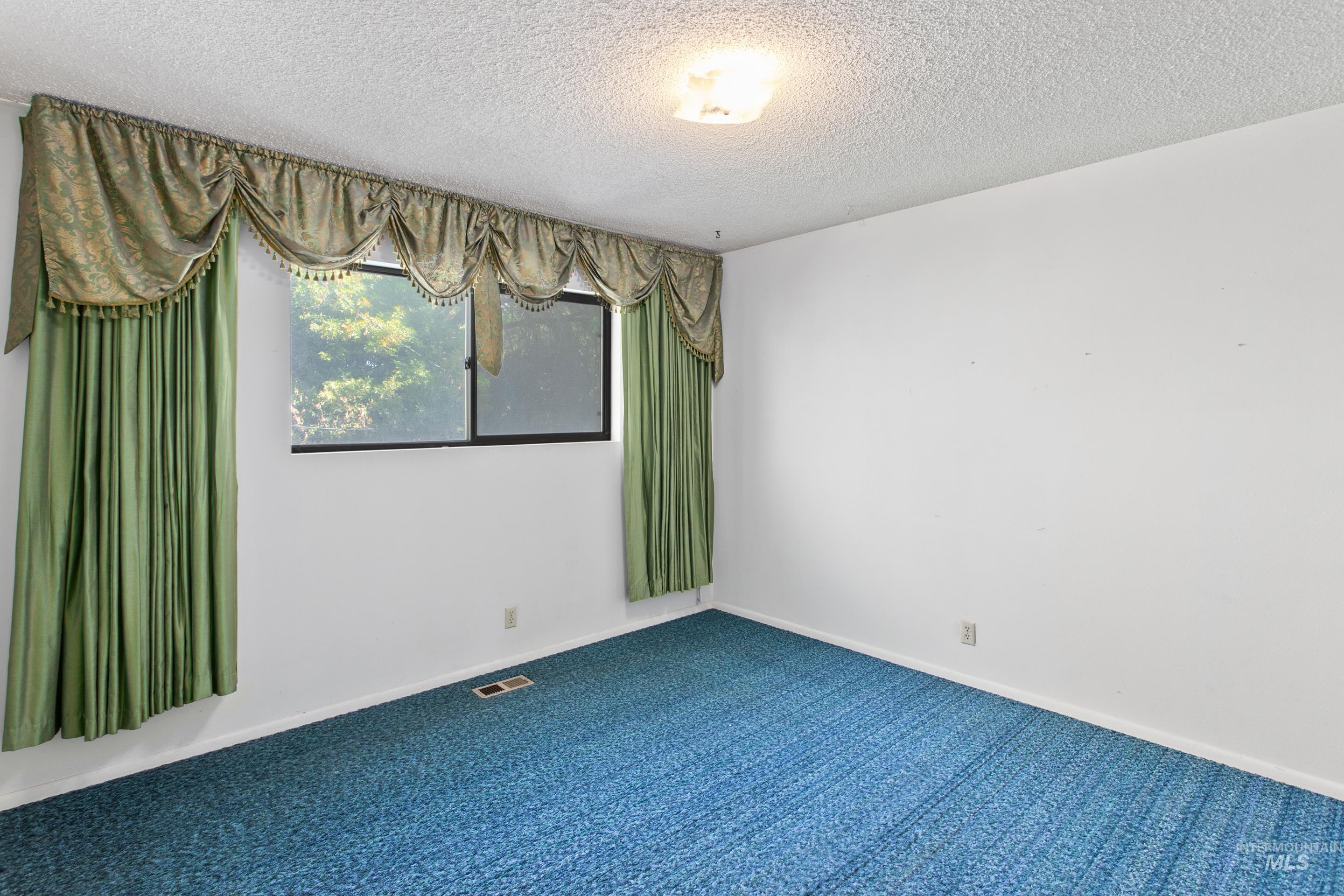 Carpeted spare room with a textured ceiling and baseboards