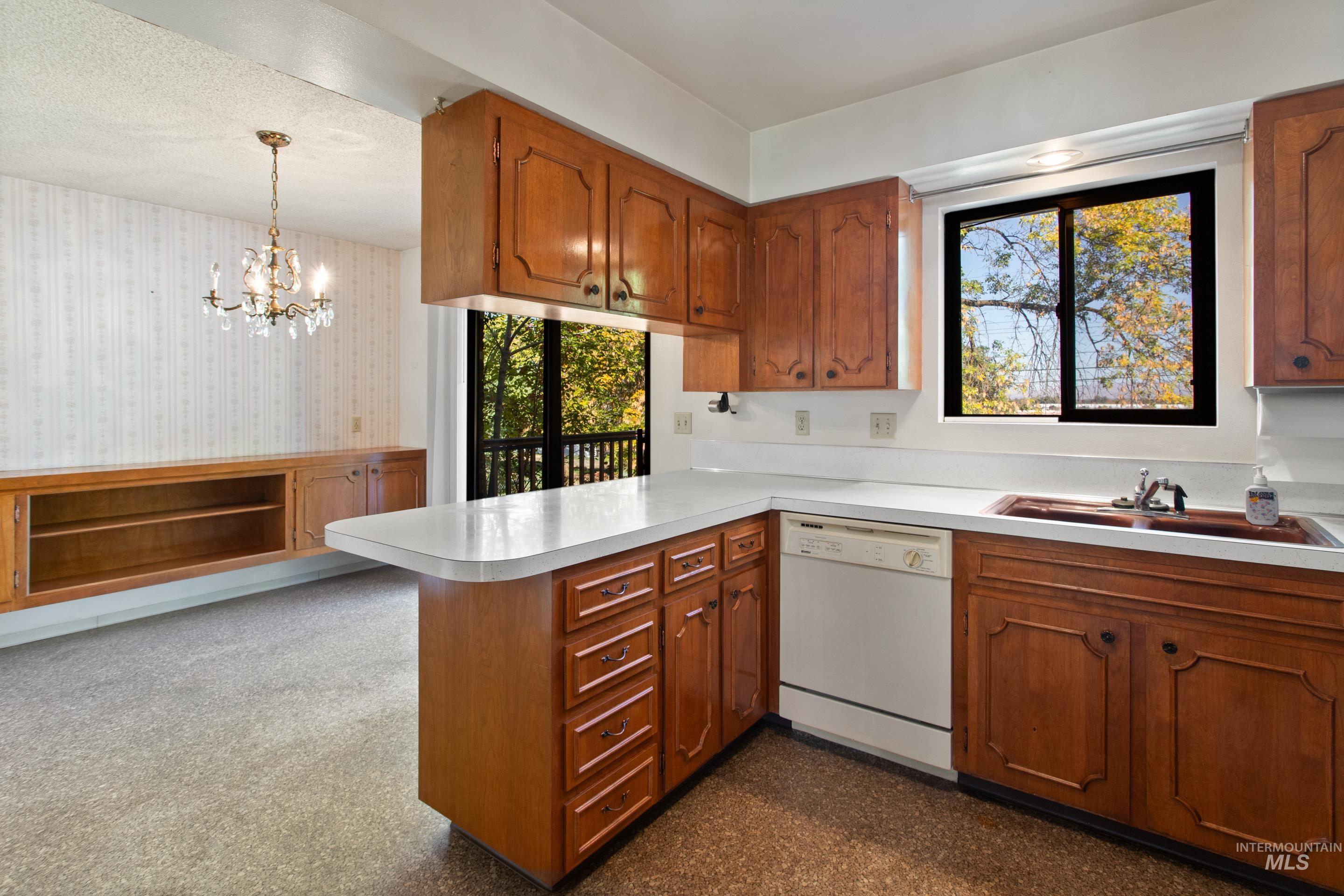 Kitchen with brown cabinetry, dishwasher, light countertops, and wallpapered walls