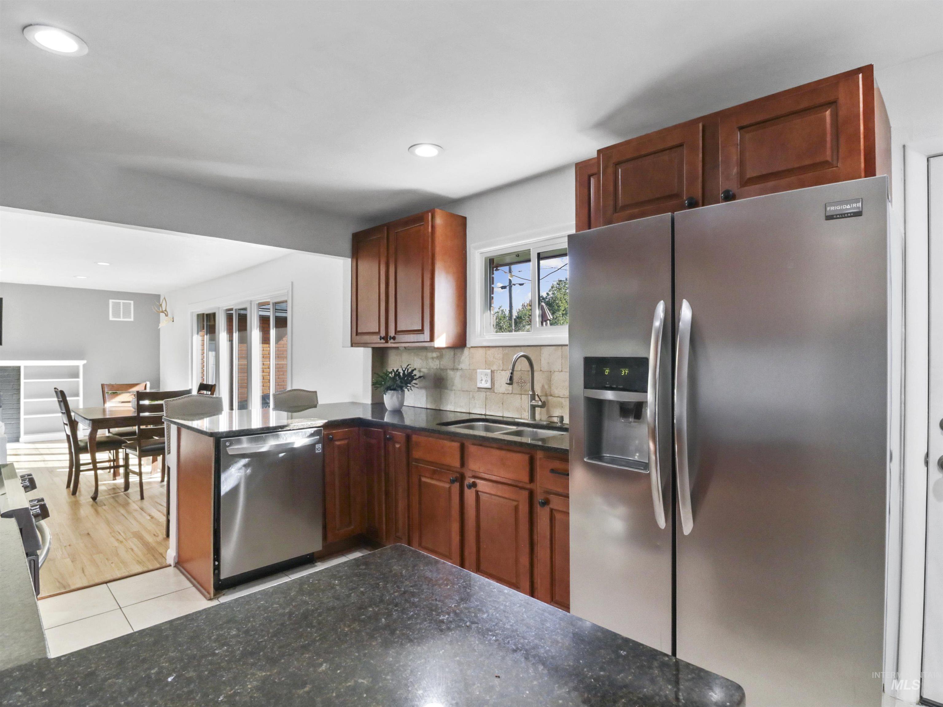 Kitchen with appliances with stainless steel finishes, decorative backsplash, a peninsula, recessed lighting, and dark stone counters