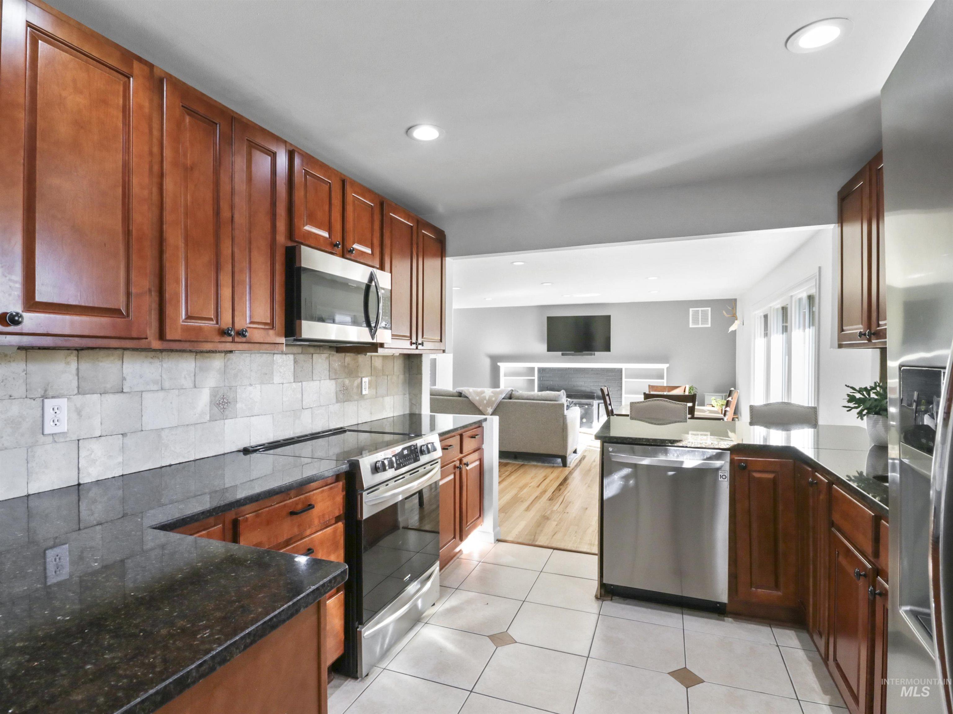 Kitchen with stainless steel appliances, a peninsula, backsplash, open floor plan, and dark stone countertops