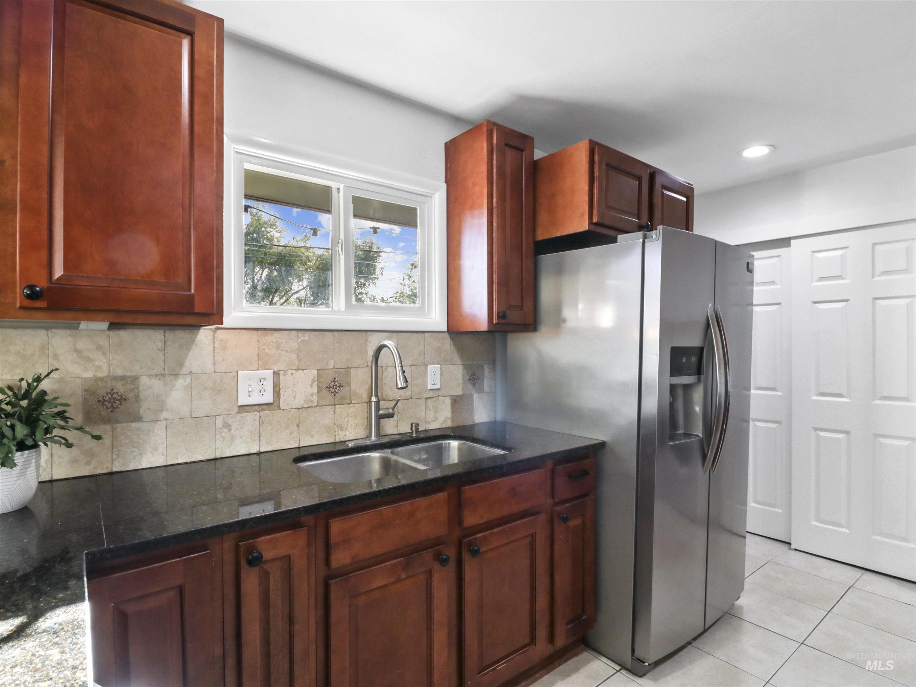Kitchen featuring tasteful backsplash, light tile patterned floors, dark stone countertops, and stainless steel fridge with ice dispenser