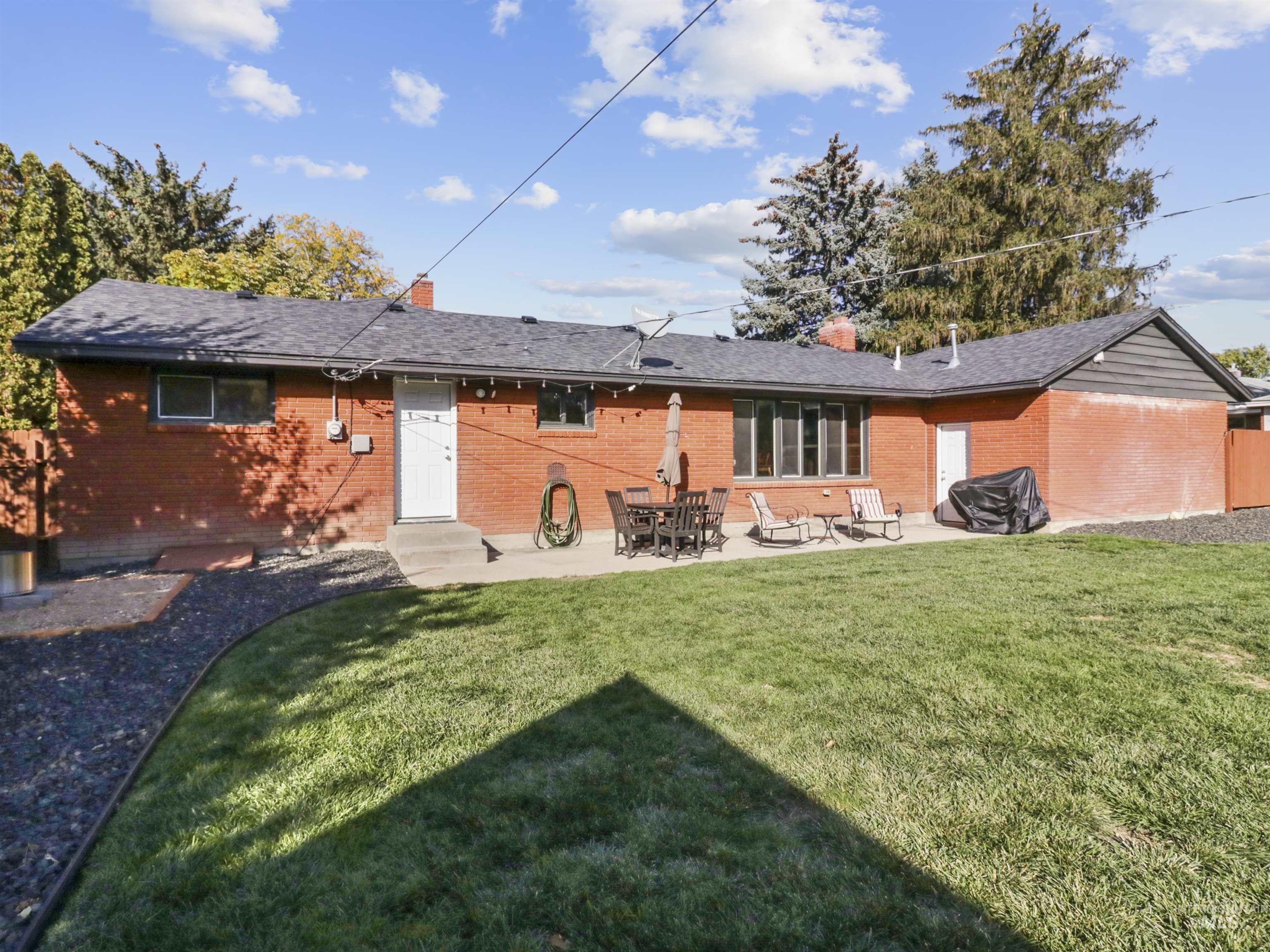 Rear view of house featuring brick siding, a chimney, a patio, a yard, and entry steps