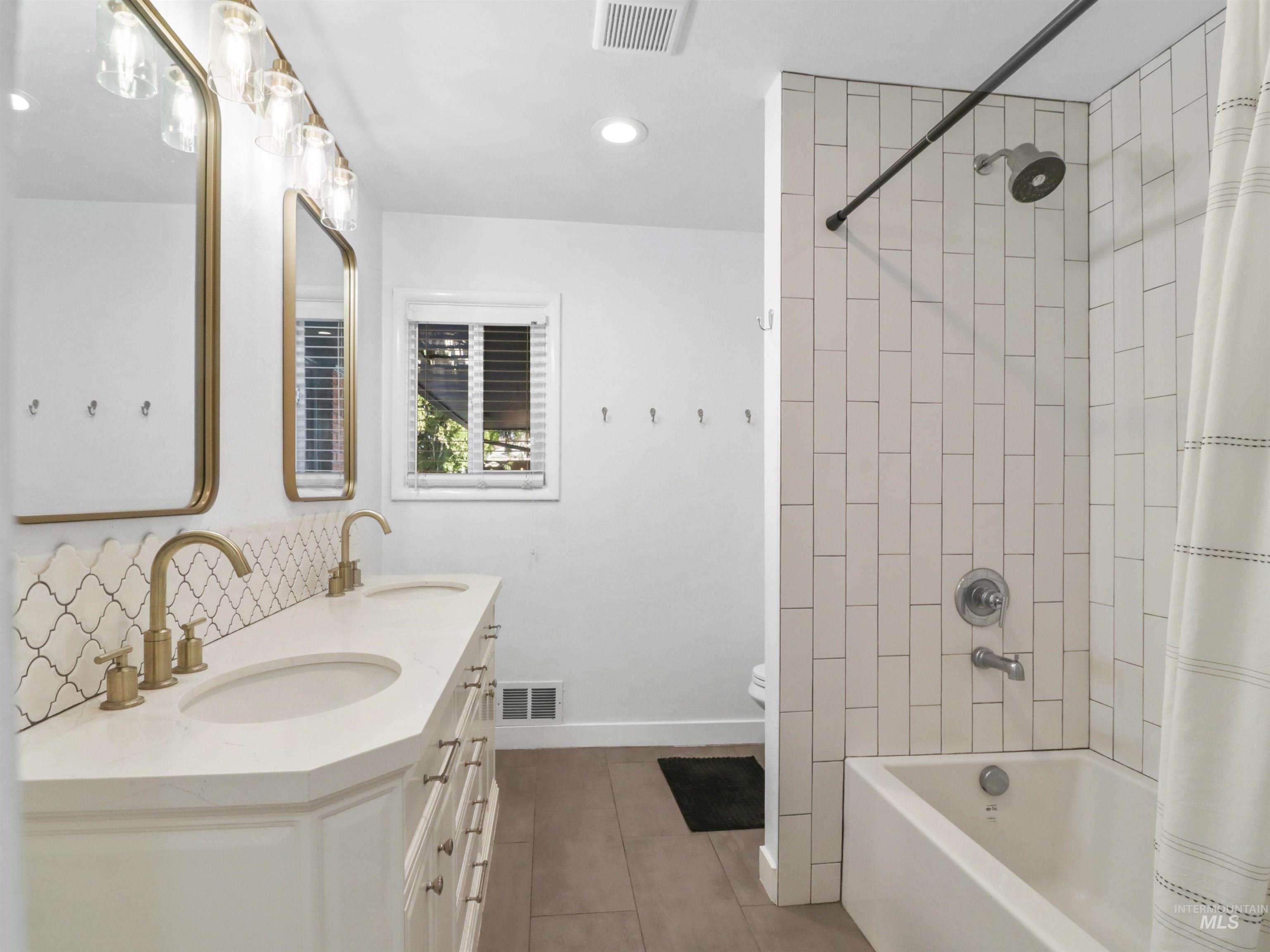 Full bath featuring shower / bath combo, double vanity, recessed lighting, tasteful backsplash, and dark tile patterned floors