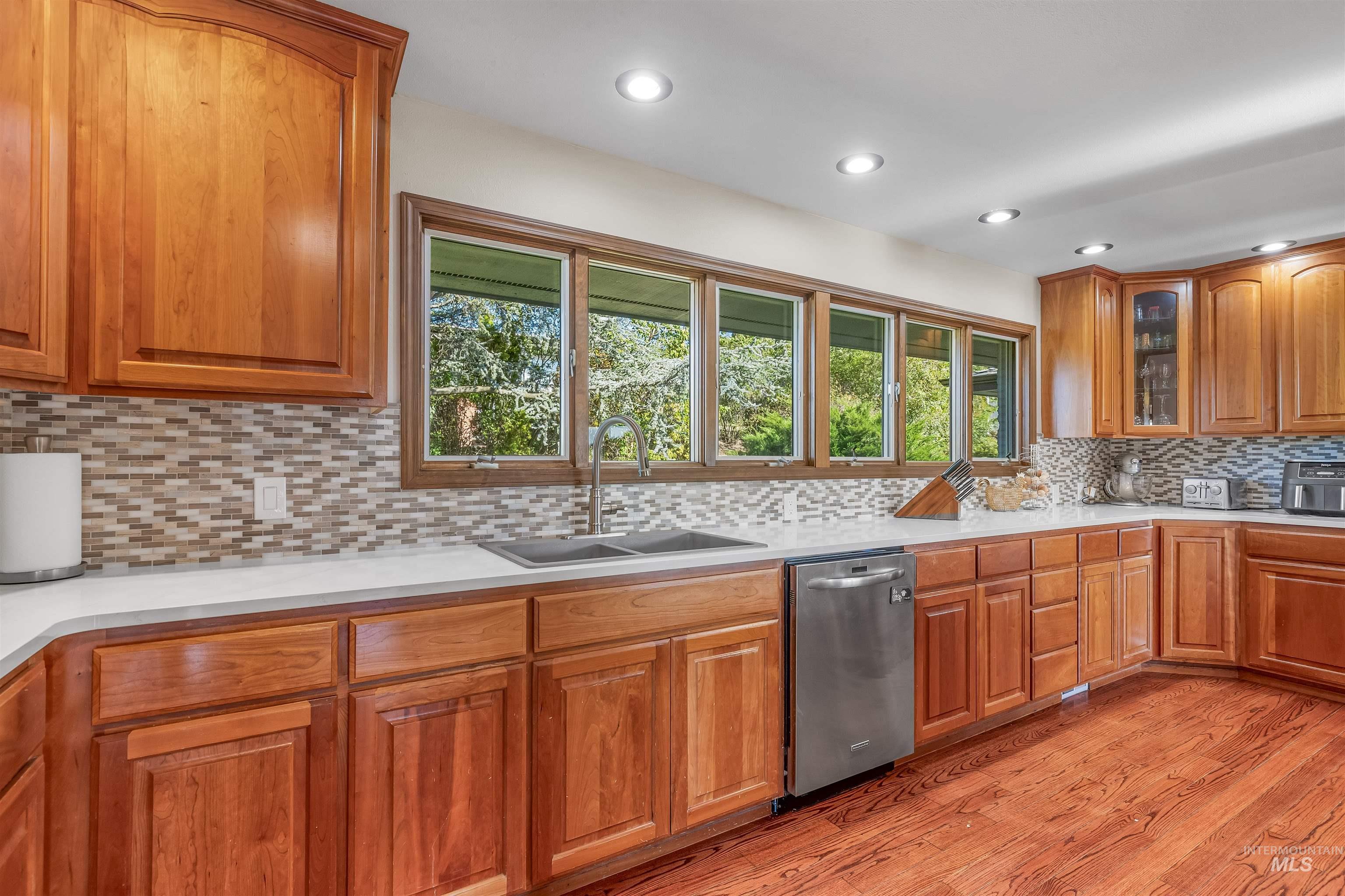 Kitchen with backsplash, brown cabinets, dishwasher, light wood-type flooring, and recessed lighting