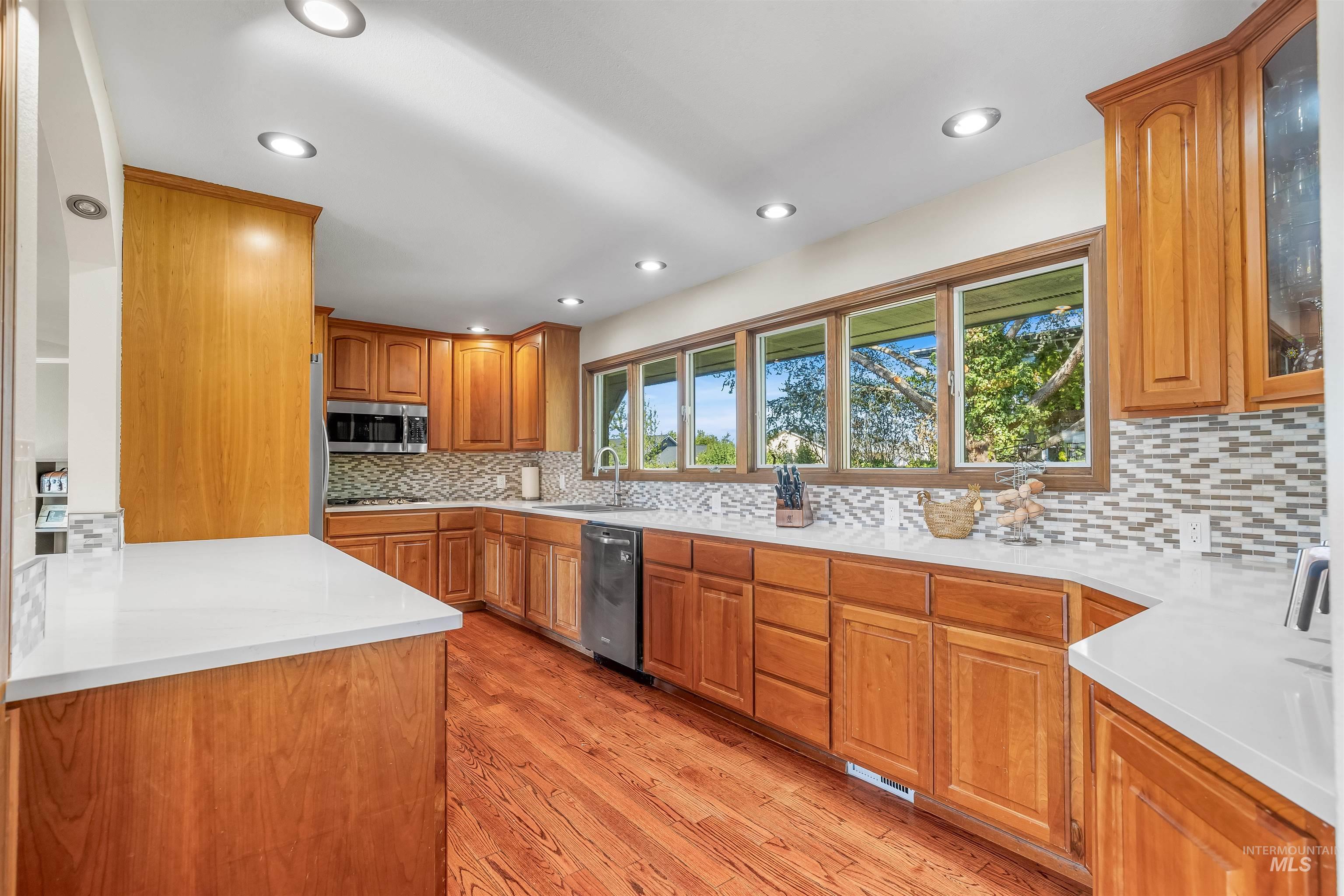Kitchen with glass insert cabinets, brown cabinets, light wood-style floors, stainless steel appliances, and recessed lighting