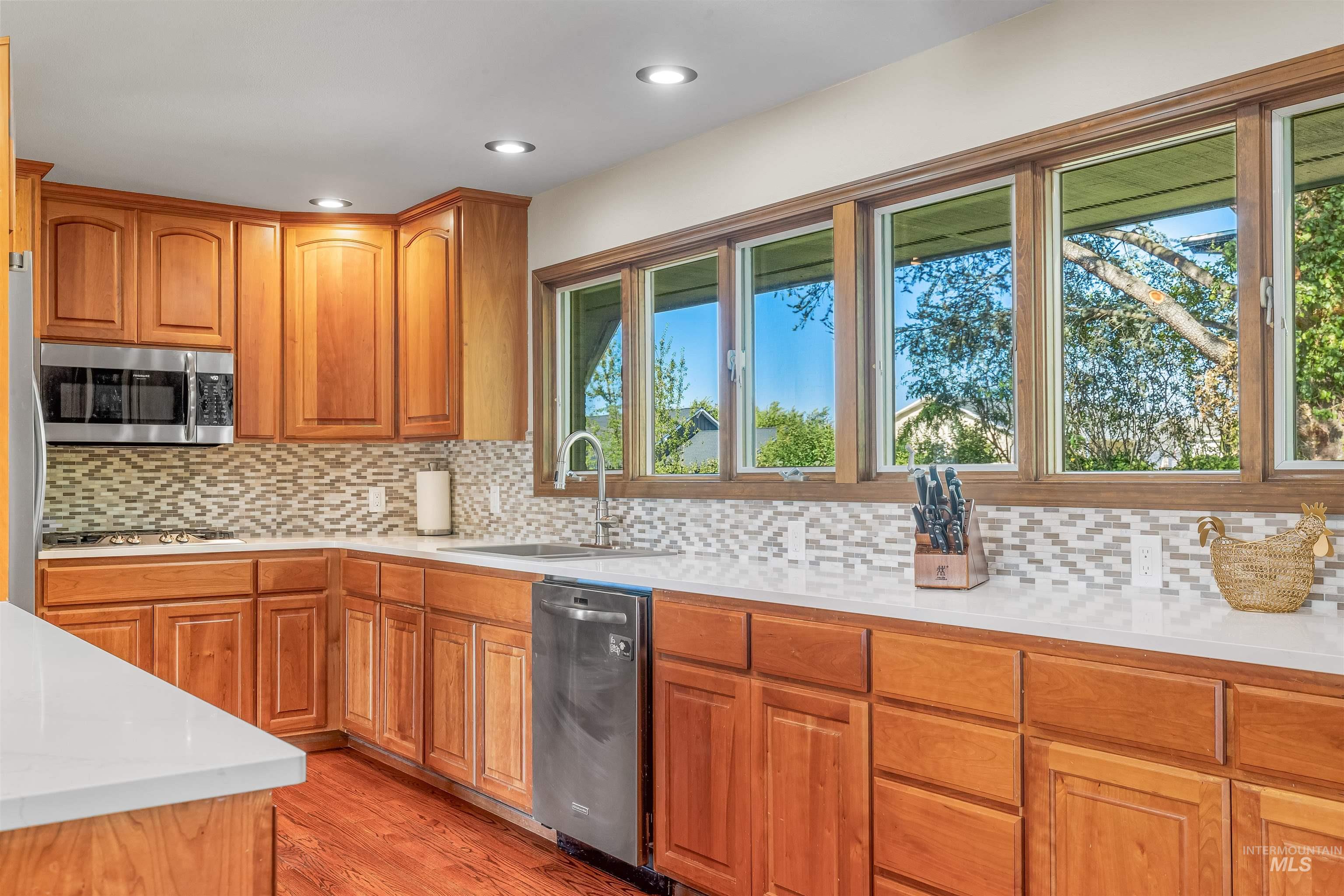 Kitchen featuring stainless steel appliances, light wood-style flooring, brown cabinets, decorative backsplash, and light stone countertops