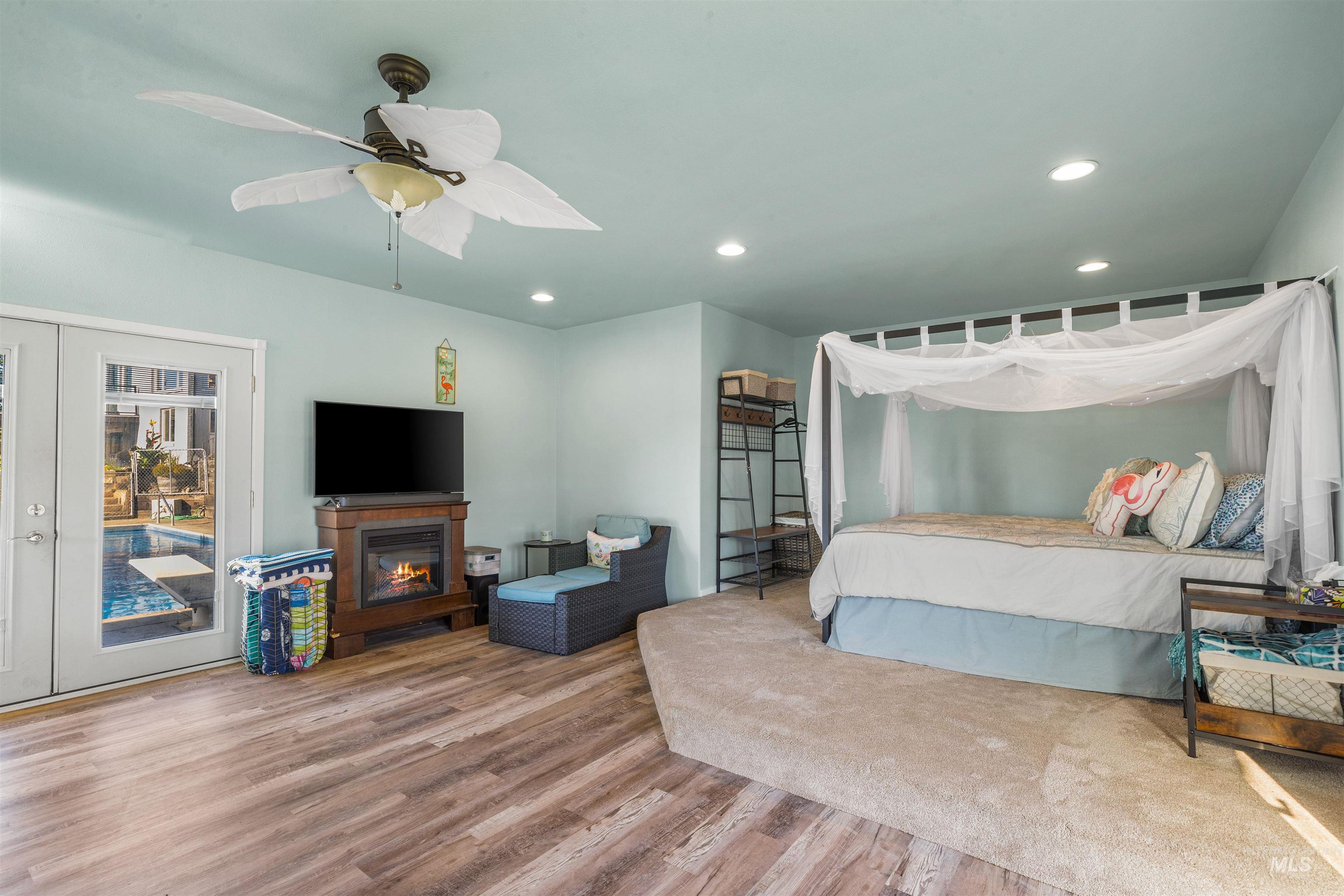 Bedroom featuring recessed lighting, wood finished floors, a glass covered fireplace, a ceiling fan, and access to exterior