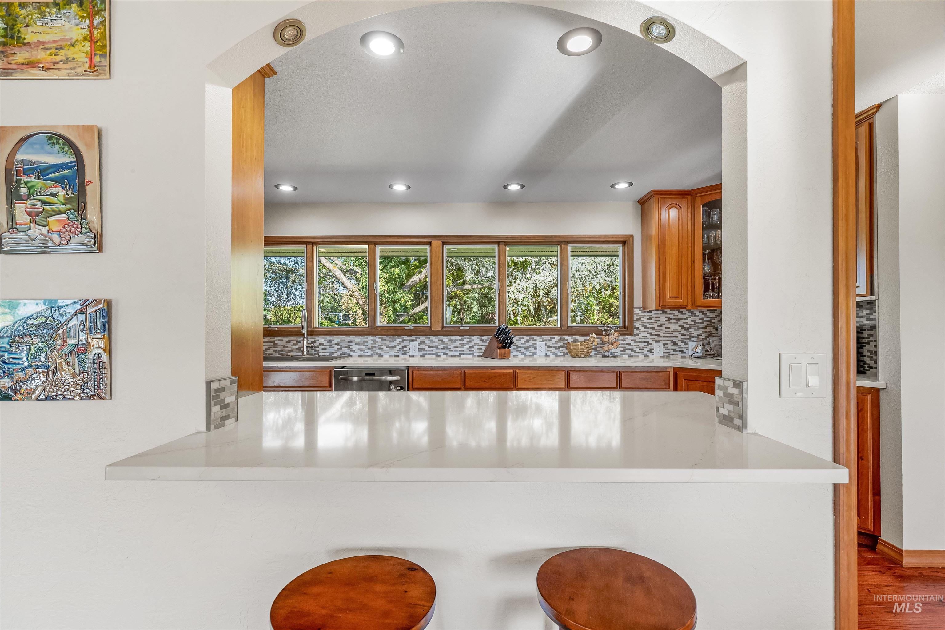 Kitchen featuring backsplash, a kitchen bar, recessed lighting, brown cabinets, and glass insert cabinets