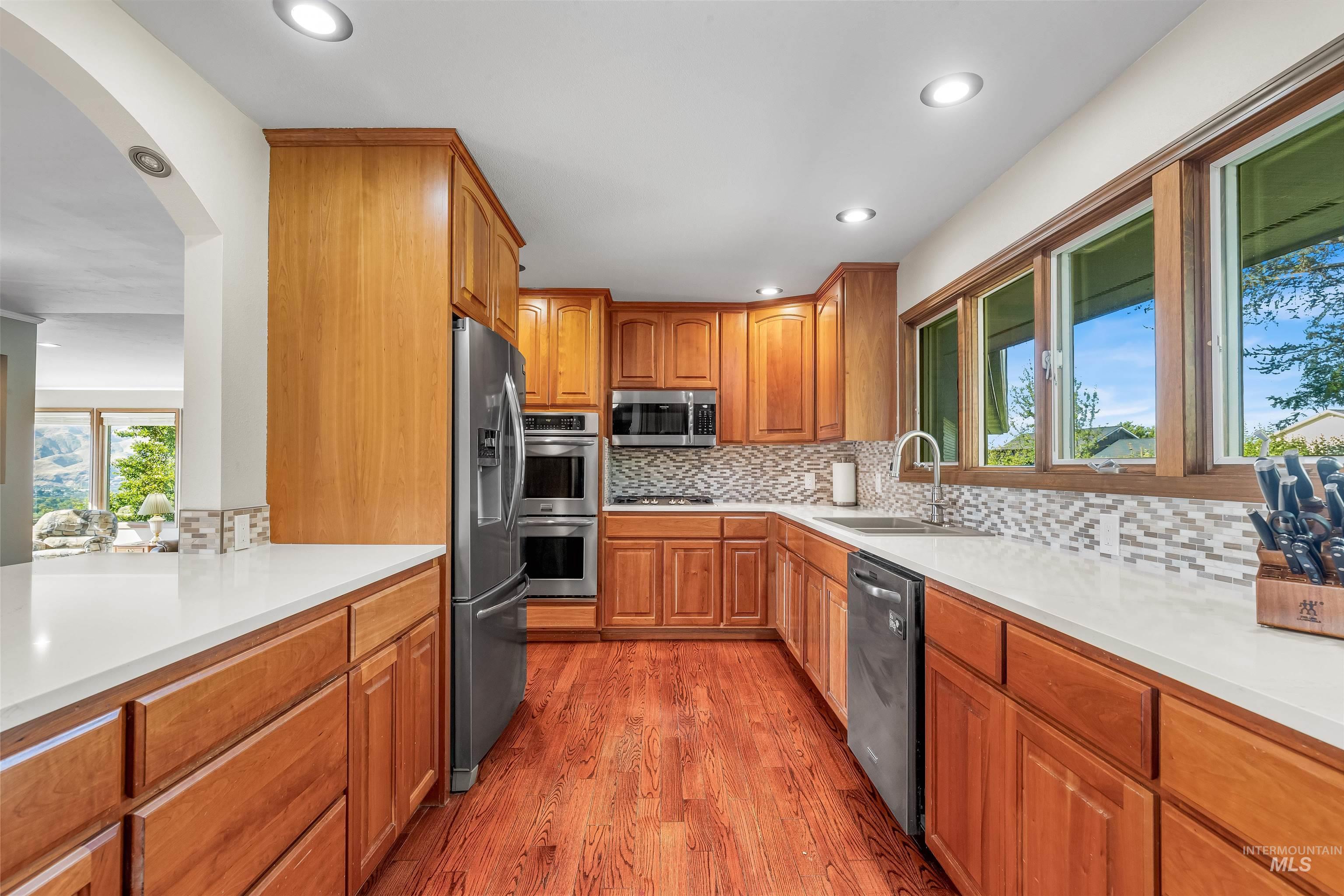 Kitchen with backsplash, arched walkways, brown cabinets, light wood finished floors, and stainless steel appliances