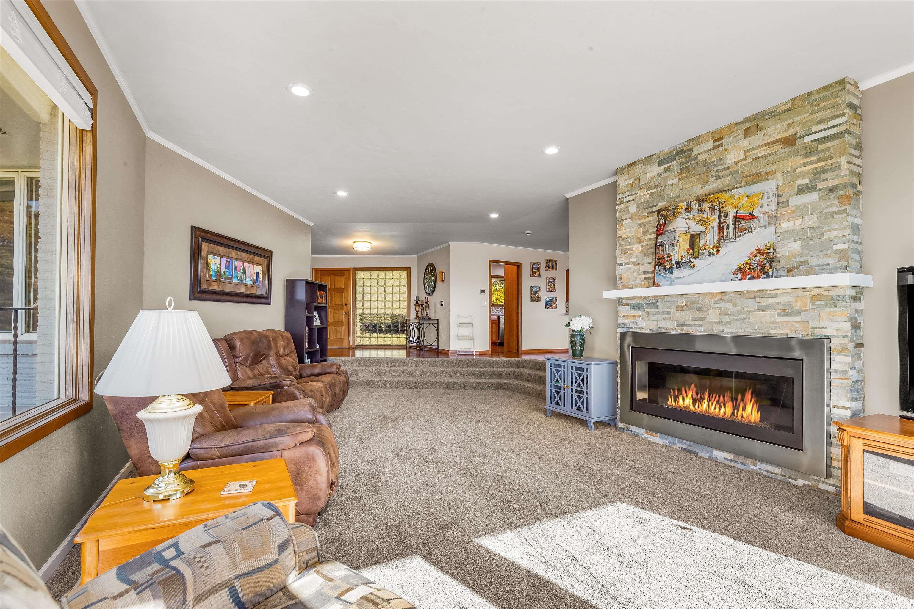 Living room with ornamental molding, a stone fireplace, recessed lighting, carpet floors, and stairway