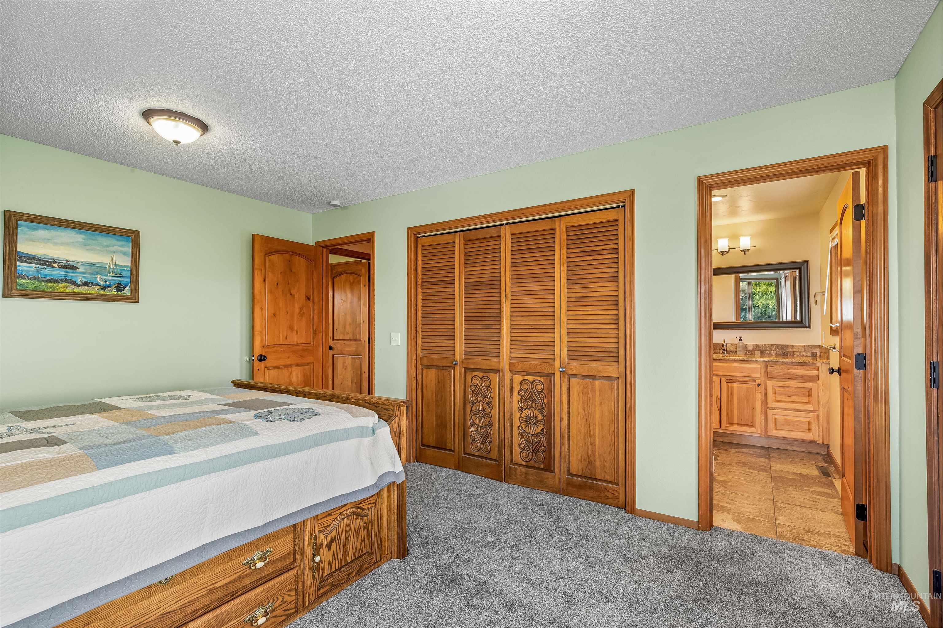 Bedroom with a textured ceiling, light carpet, a closet, and ensuite bath