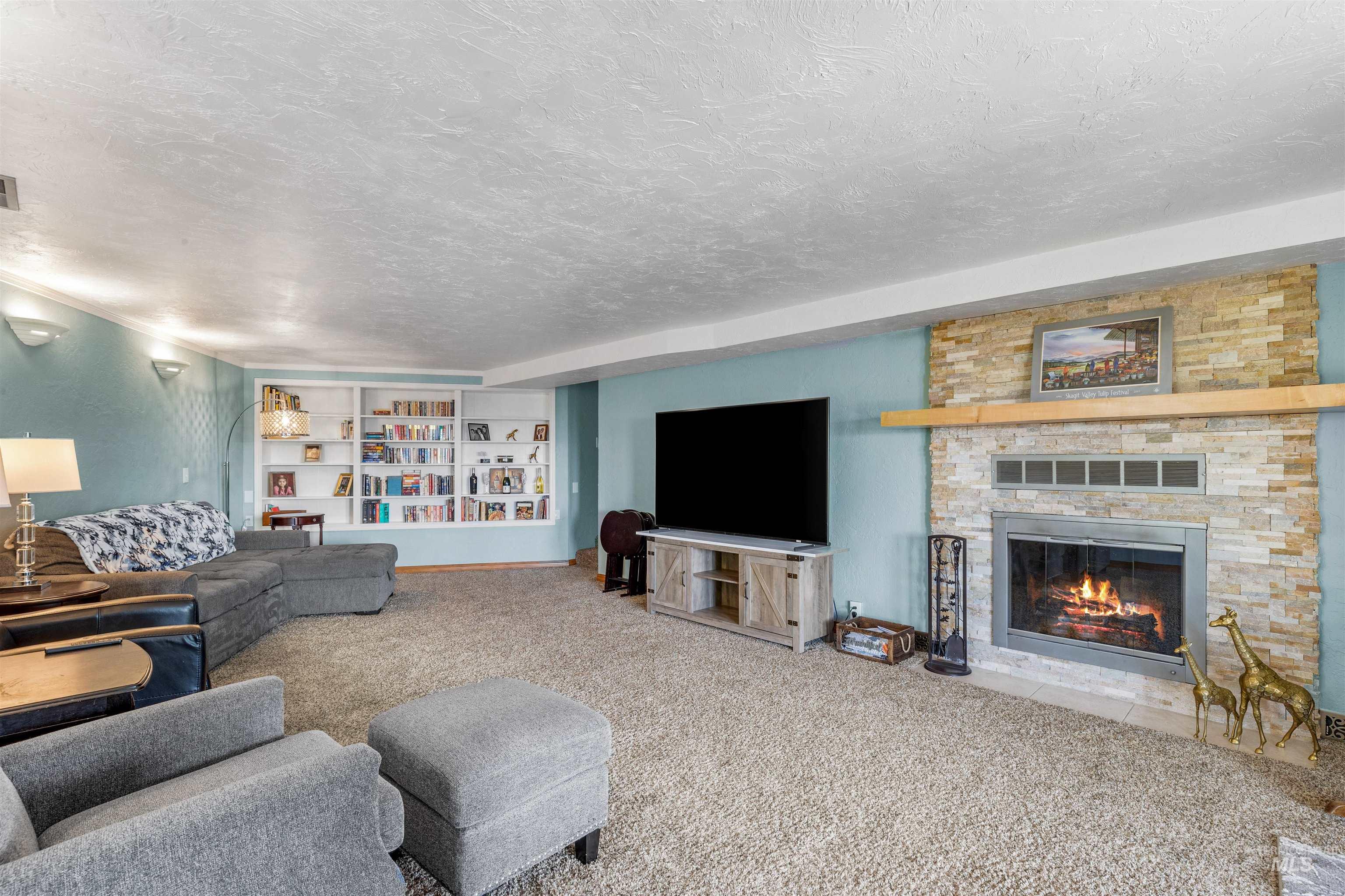 Living room featuring carpet, a stone fireplace, and a textured ceiling