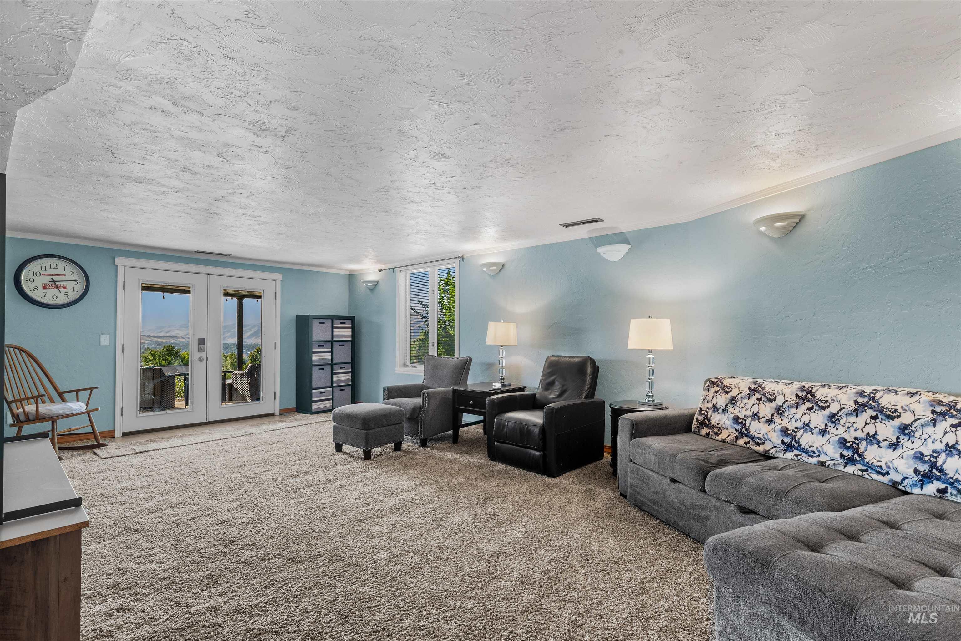 Living area featuring light carpet, a textured ceiling, a textured wall, and french doors