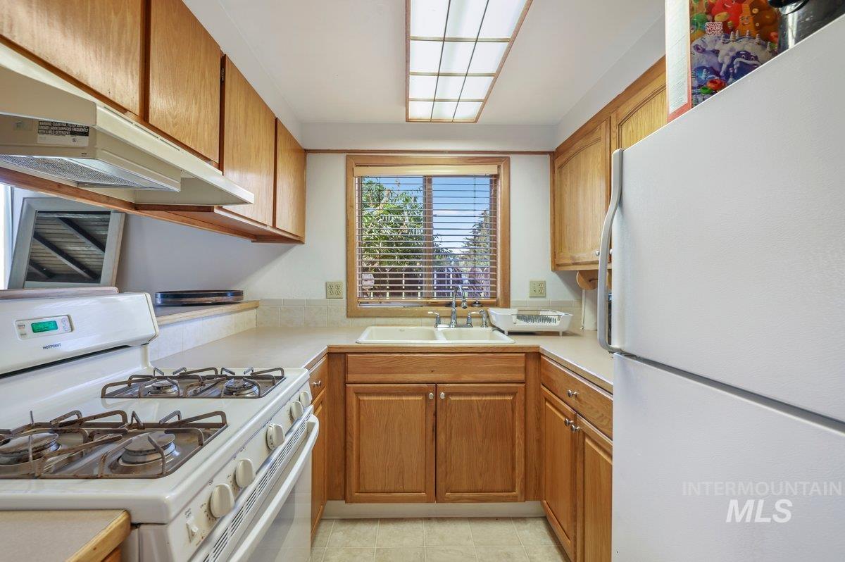 Kitchen featuring white appliances, light countertops, brown cabinetry, and under cabinet range hood