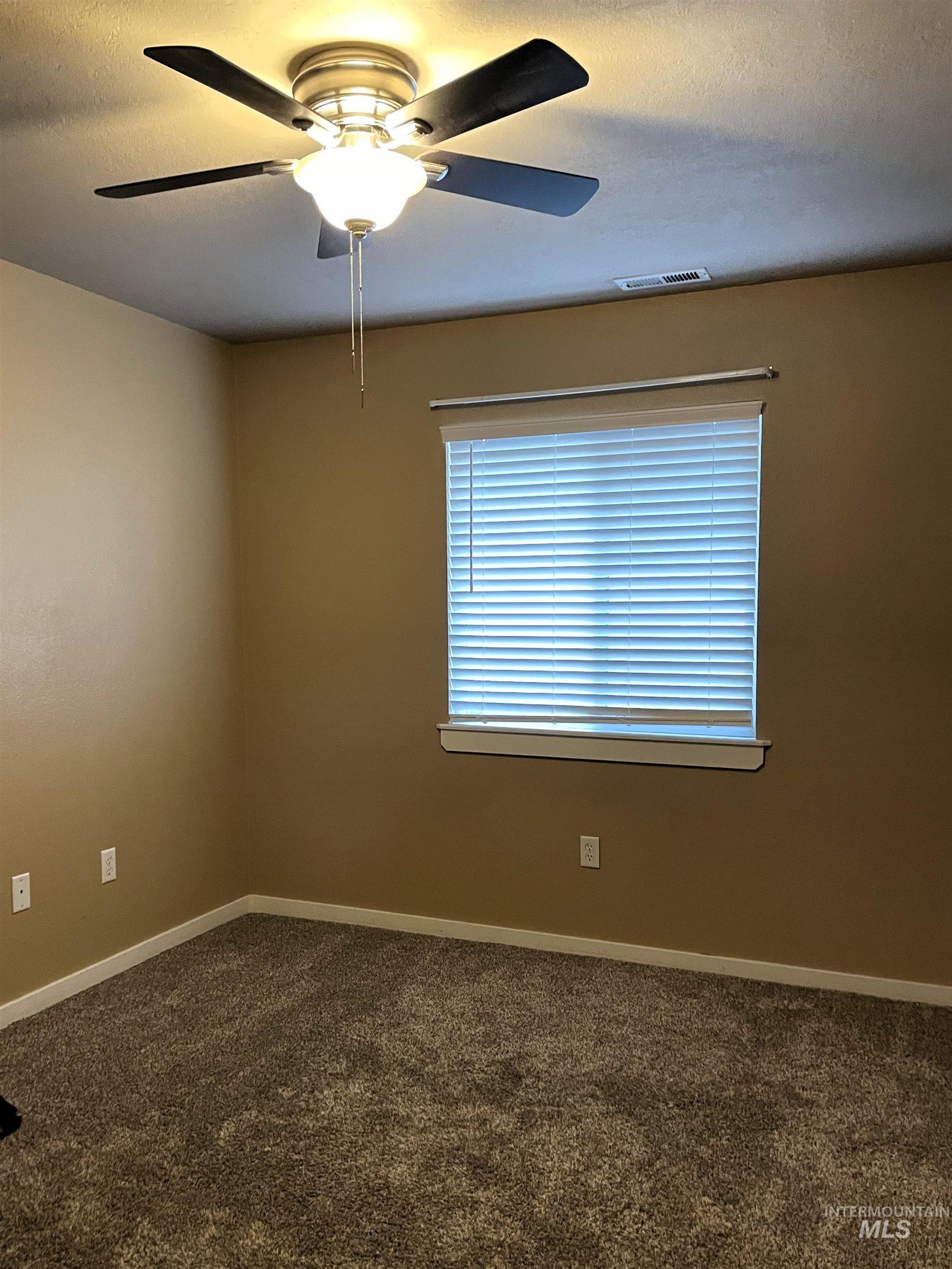 Neutral-toned interior room with textured carpeting, a window with horizontal blinds, and a ceiling fan with integrated lighting