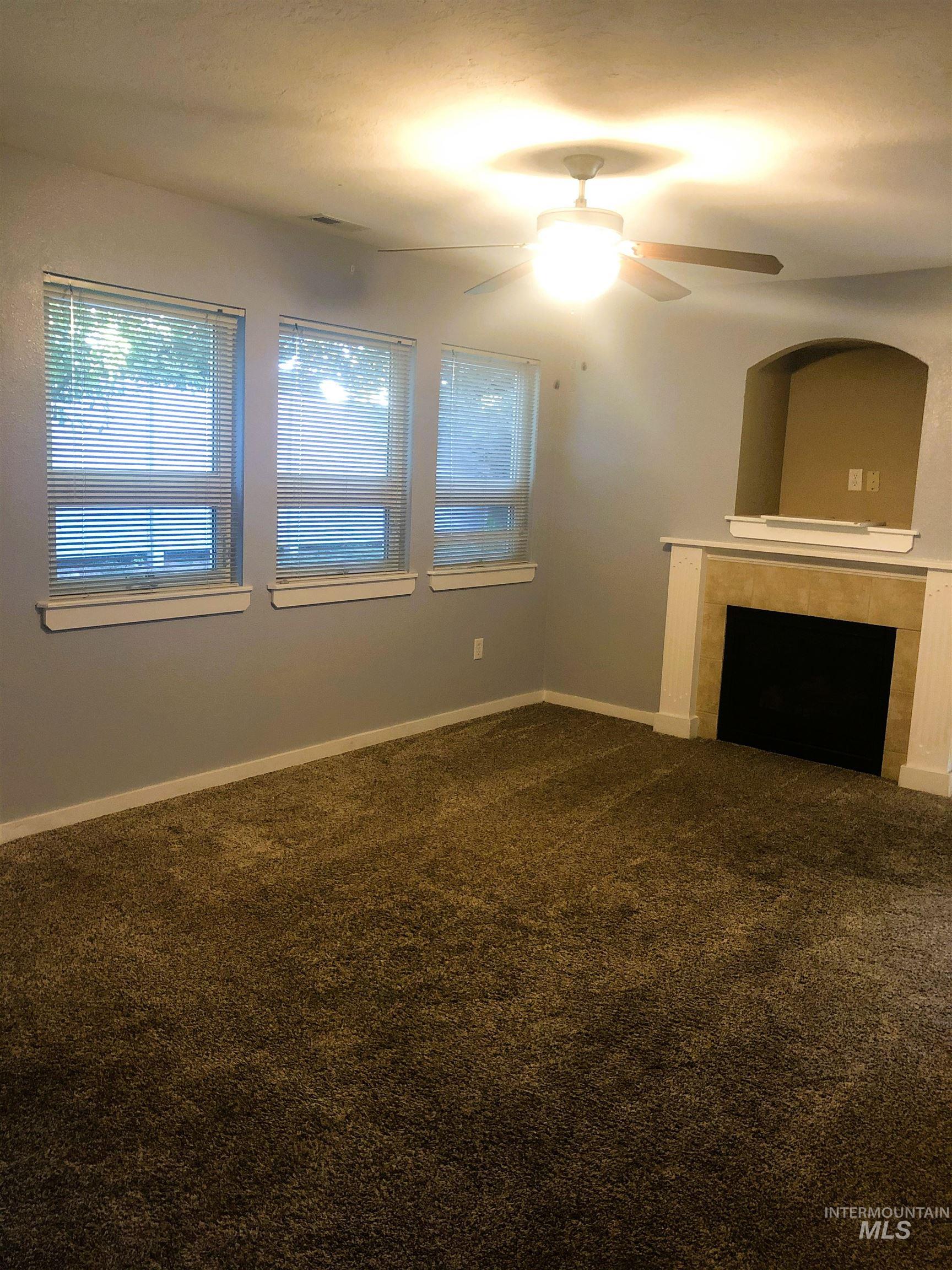 Living space featuring a fireplace with a mantel, an arched alcove, three windows with blinds, a ceiling fan with integrated lighting, and carpeted flooring