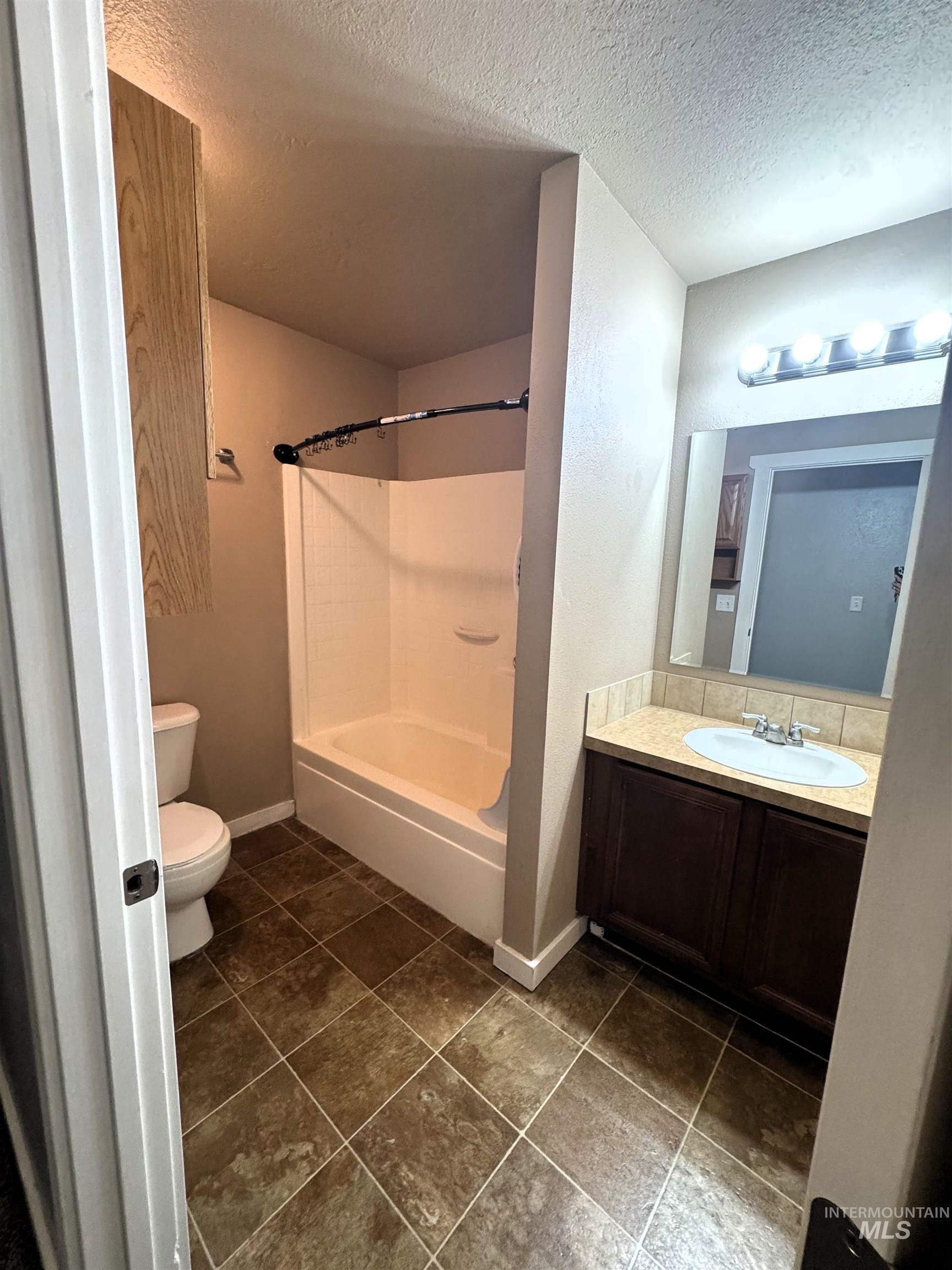 Bathroom featuring a shower-over-tub combination, a vanity with a single sink, wood-finish cabinetry, a neutral countertop, and tiled flooring