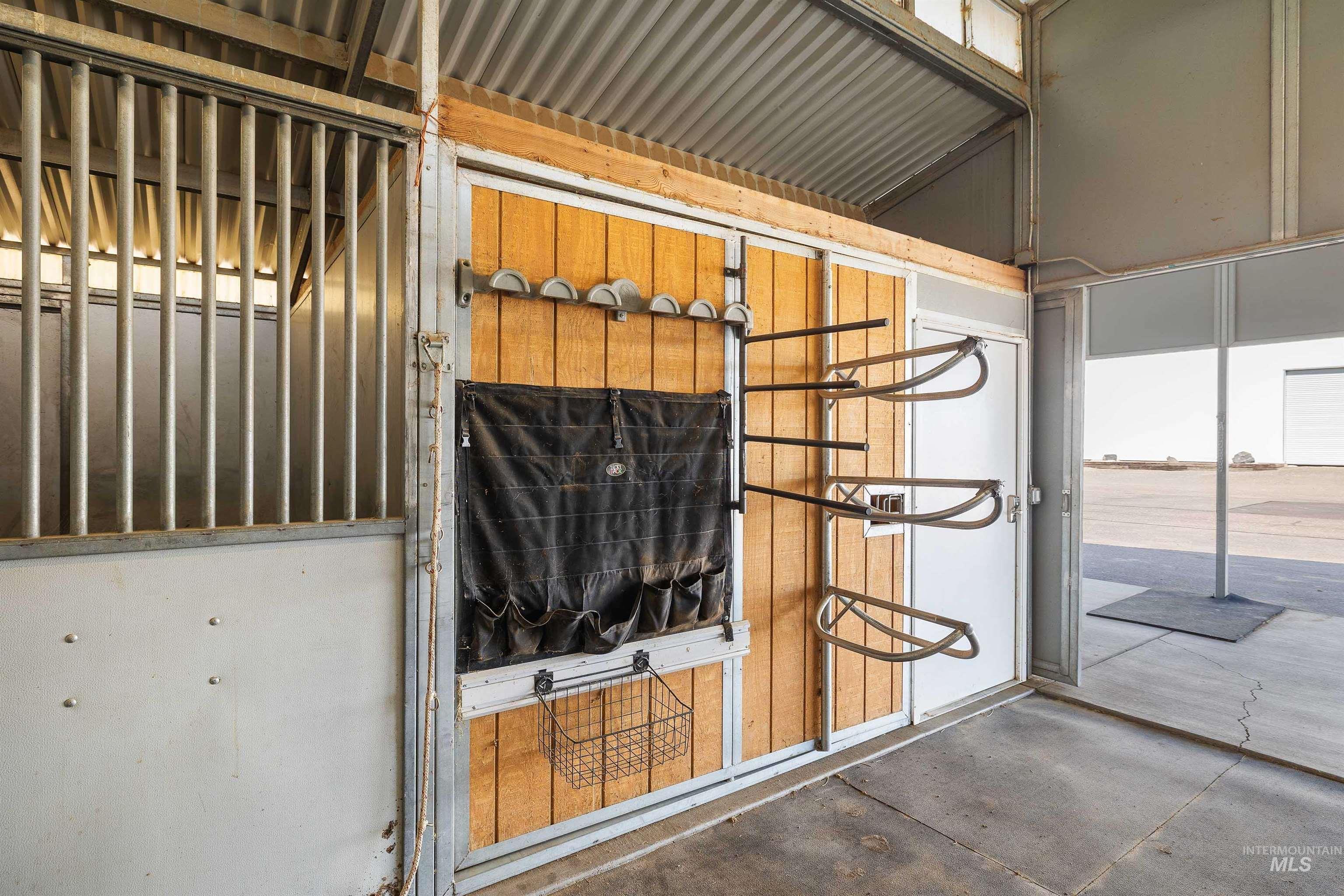 Equine facility stall featuring wood paneling, metal grating, a white door, and saddle racks