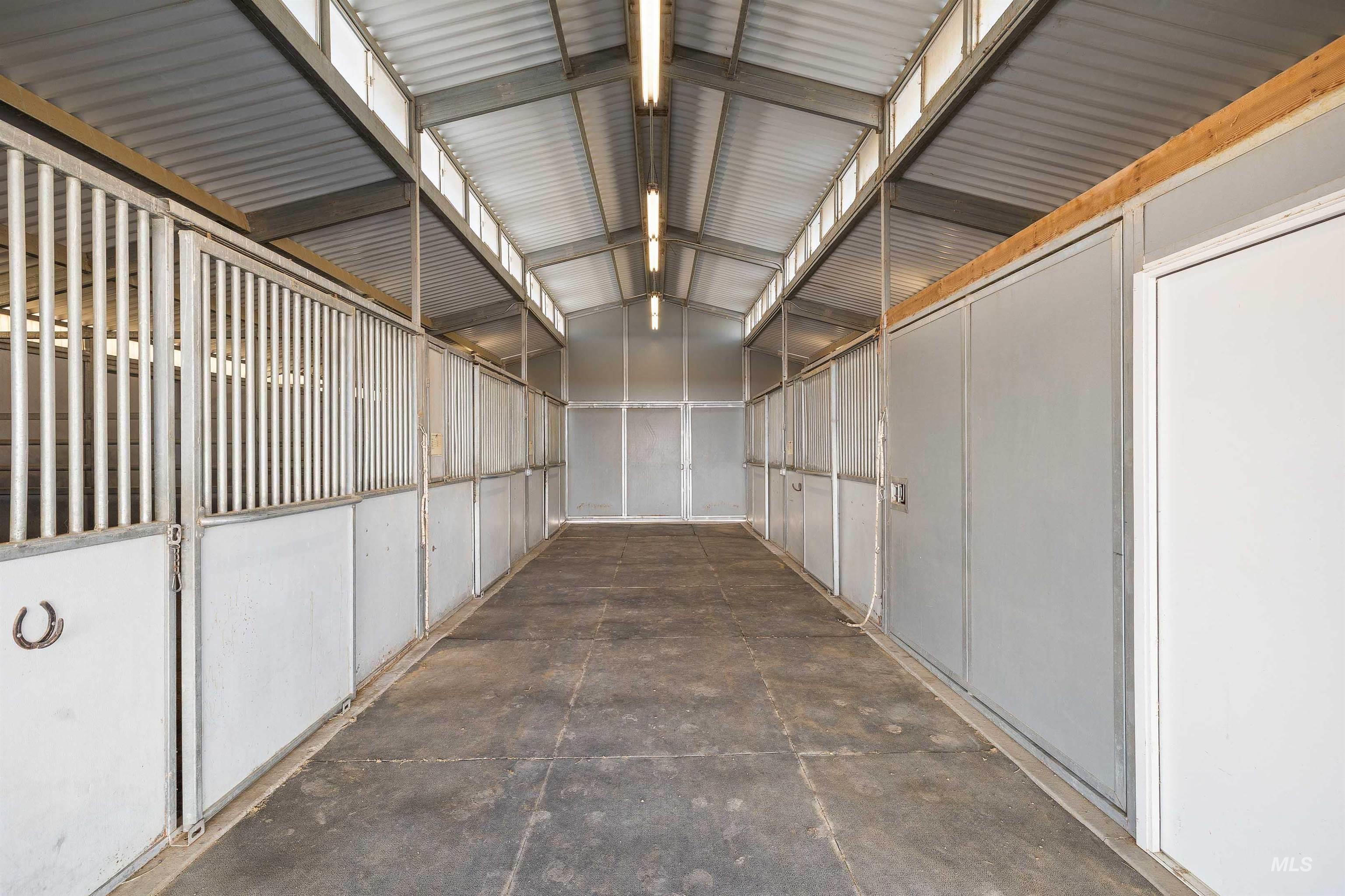 Enclosed barn aisle featuring multiple stalls with metal bar tops and solid lower panels