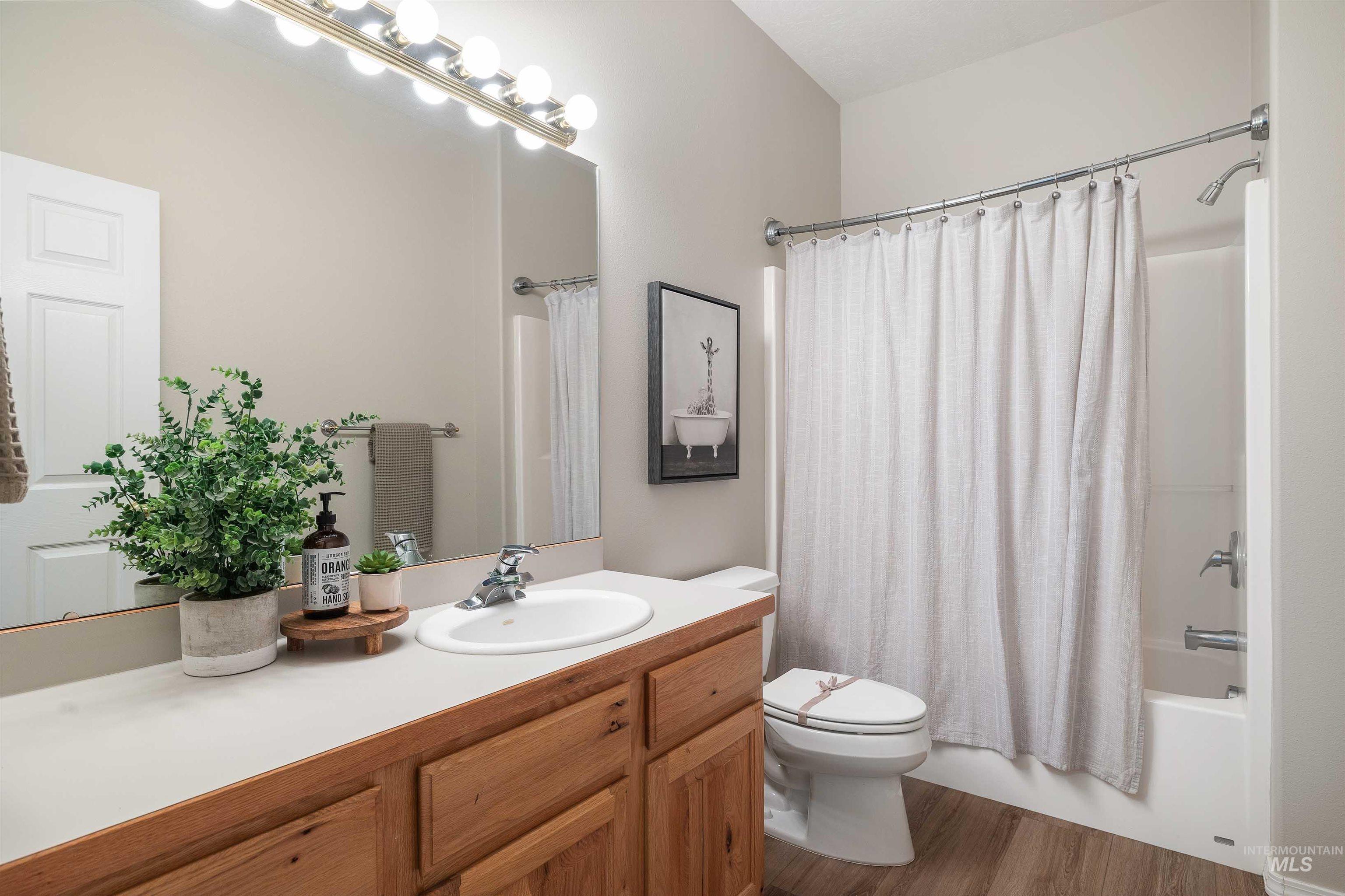 Bathroom featuring a single vanity with a white countertop, wood-finish cabinetry, a large mirror, and a full shower/tub combination
