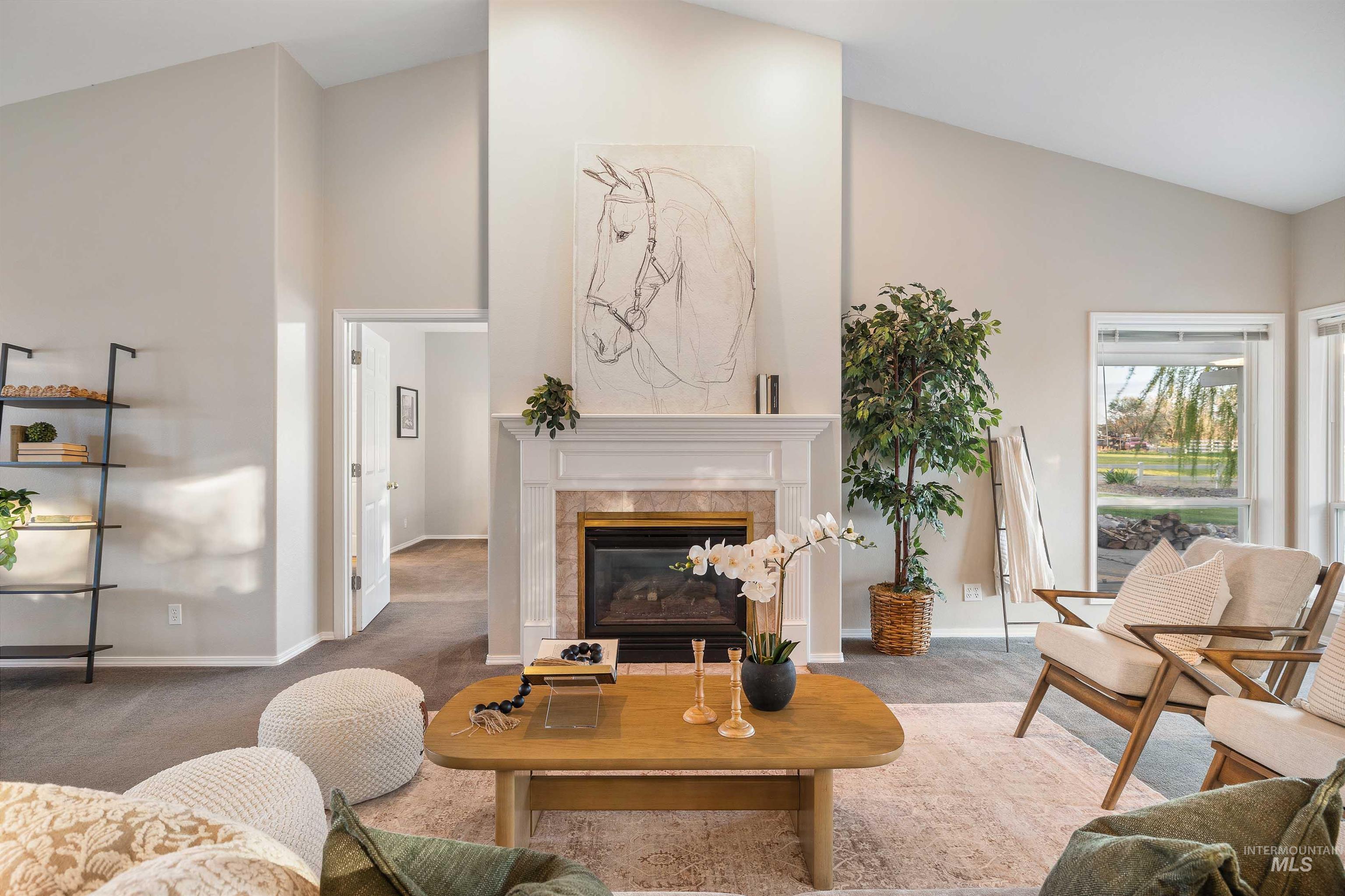 Spacious living area featuring a vaulted ceiling, a fireplace with a white mantel and tile surround, and large windows