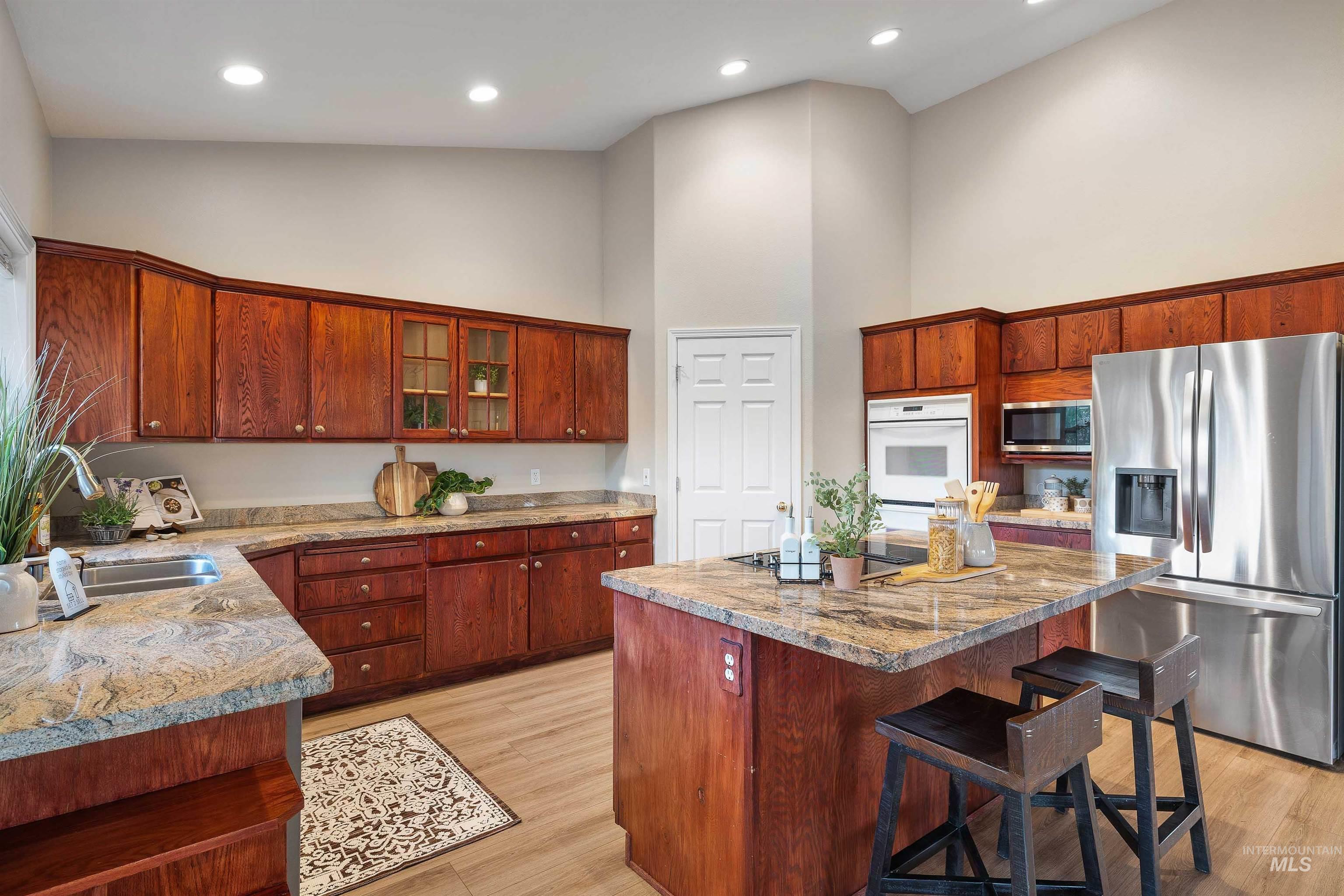 Kitchen featuring wood-finish cabinetry, light-toned countertops, stainless steel appliances, a center island with bar seating, and recessed lighting