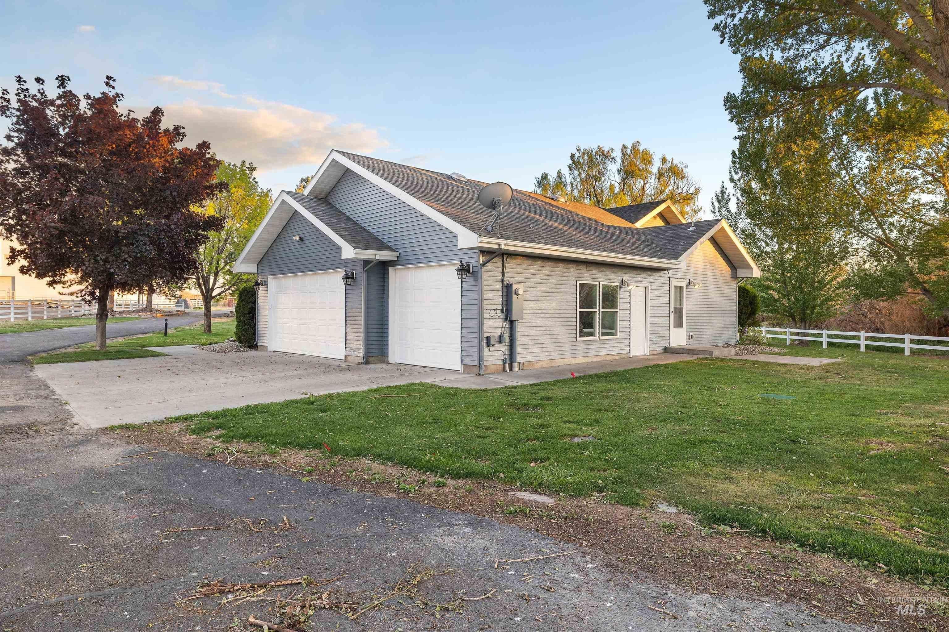 Exterior featuring light blue siding, a two-car garage with white doors, a white picket fence, and a concrete patio