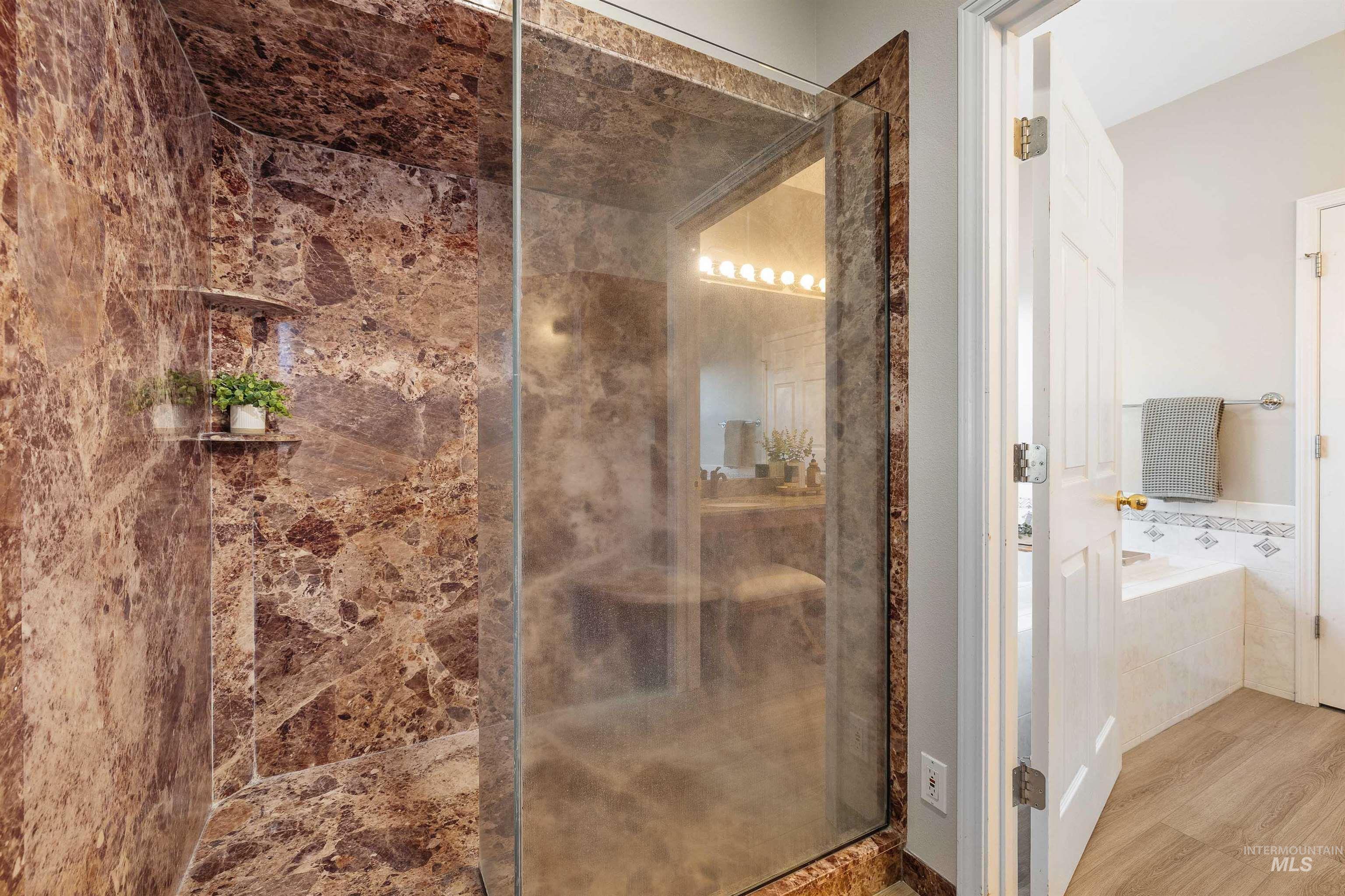 Glass-enclosed shower featuring full-height natural stone-patterned walls and a built-in shower niche