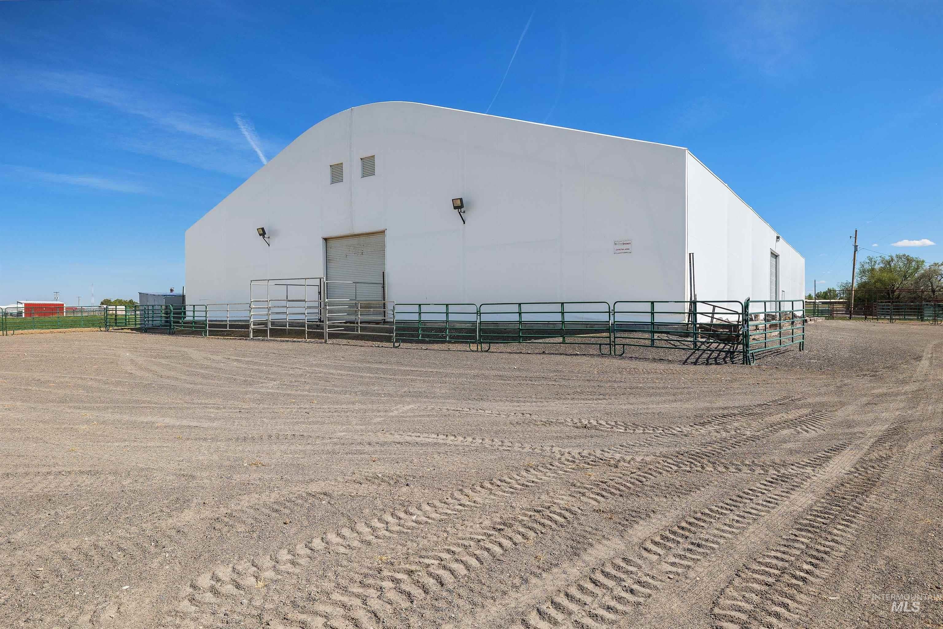 Large white arched structure featuring a prominent roll-up door, exterior lighting, and perimeter fencing