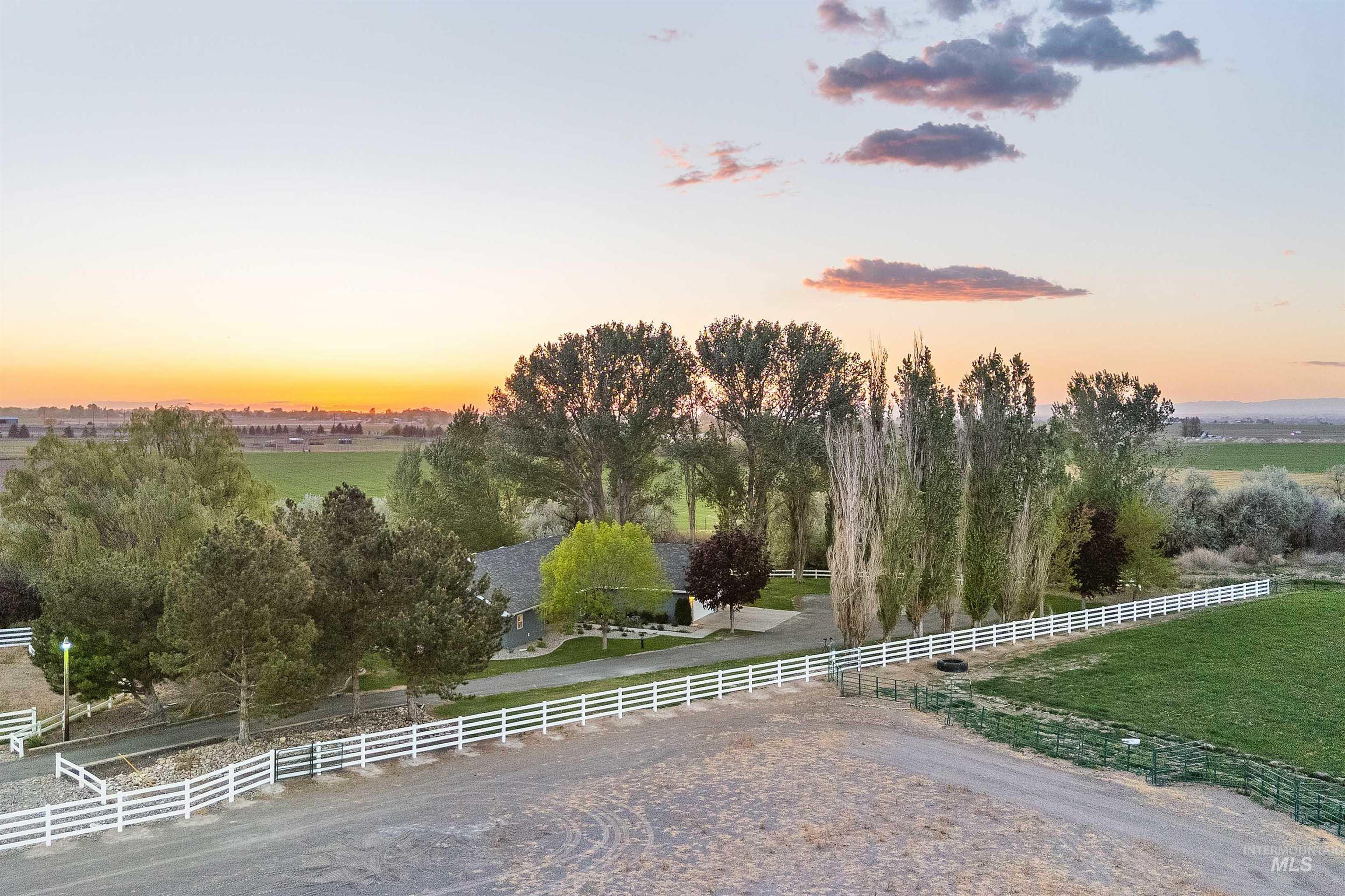 Expansive property featuring a white rail fence, a gravel driveway, and mature trees
