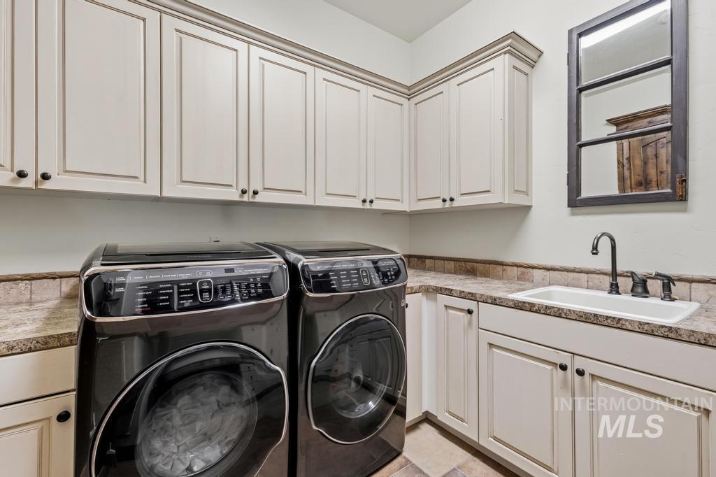 Laundry room featuring extensive upper and lower cabinetry, a built-in sink with a dark bronze faucet, and a granite countertop with a tile backsplash