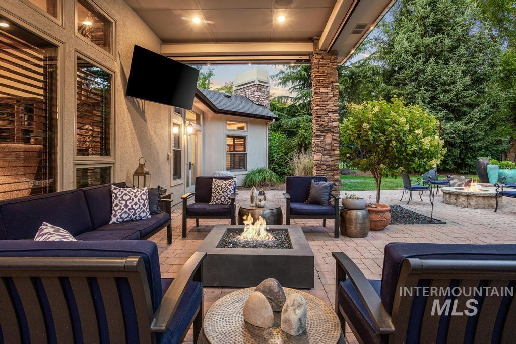 Covered outdoor patio featuring a built-in fire pit, mounted television, stacked stone column, and brick paver flooring