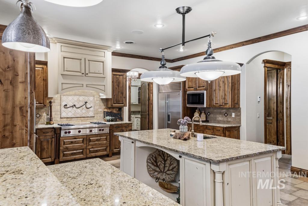 Spacious kitchen featuring an expansive island with a light-toned countertop, wood-finish cabinetry, stainless steel appliances, and decorative pendant lighting