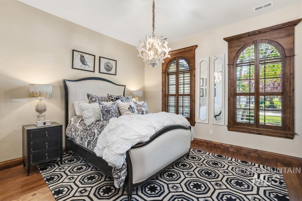 Hardwood flooring grounds this space, featuring two arched windows with custom wood trim and plantation shutters