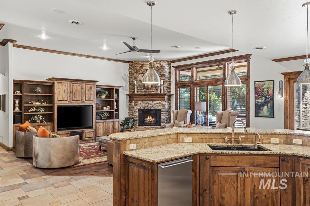 Open-concept kitchen and living area featuring a stone-clad fireplace, wood-finish built-in shelving, a kitchen island with granite countertops, and wood-framed windows