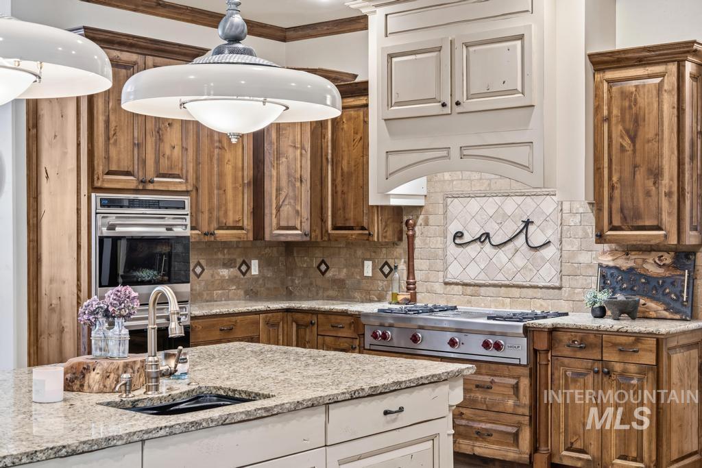Gourmet kitchen featuring a stainless steel gas range, built-in oven, stone countertops, custom cabinetry, and a tile backsplash