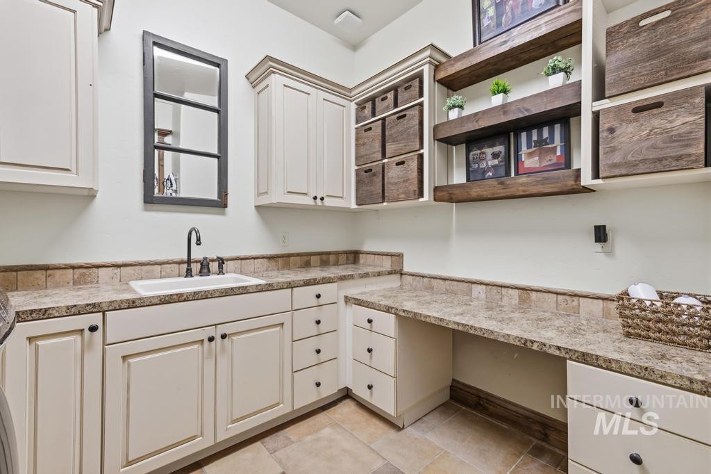 Functional utility room featuring extensive built-in cabinetry, an integrated sink with a high-arc faucet, durable granite countertops, and an open desk area