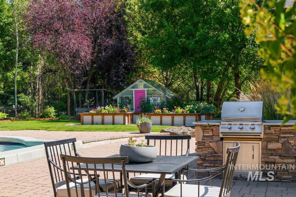 Outdoor kitchen featuring a built-in stainless steel grill with stone veneer surround, a paver patio, and a swimming pool