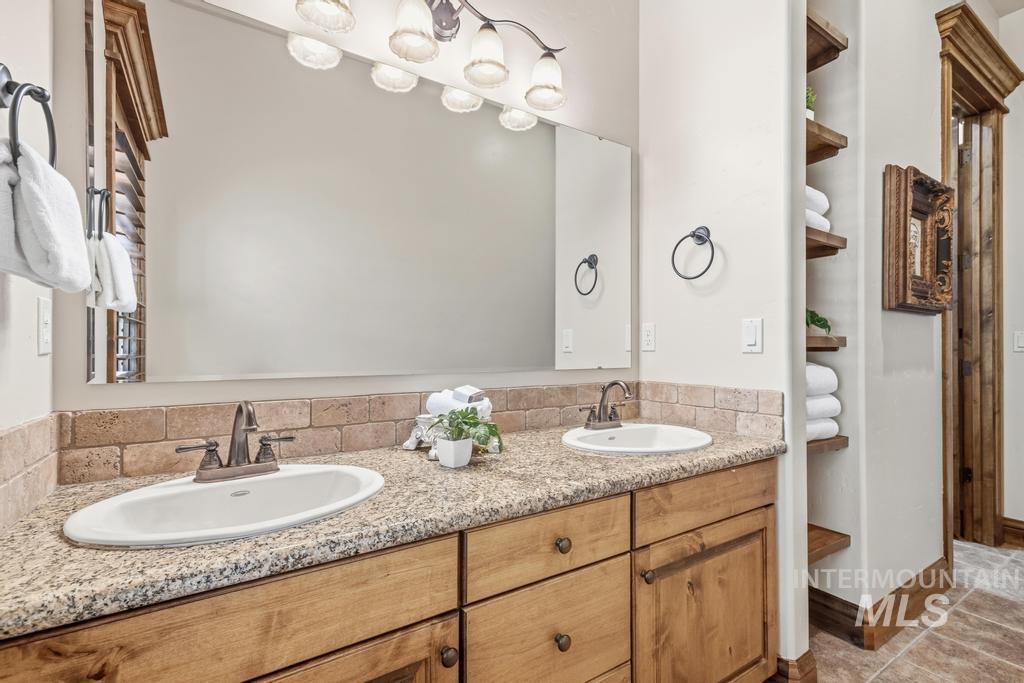 Bathroom vanity featuring dual sinks, a granite-finish countertop, and a tiled backsplash