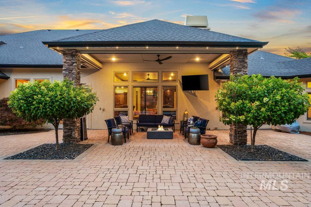 Expansive paver patio with a covered outdoor living area featuring stone-clad pillars, recessed lighting, and a ceiling fan