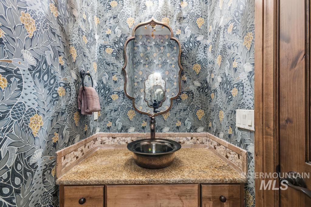 Powder room featuring a decorative wall covering, a vanity with granite countertop and mosaic tile trim, and a vessel sink with a dark bronze faucet