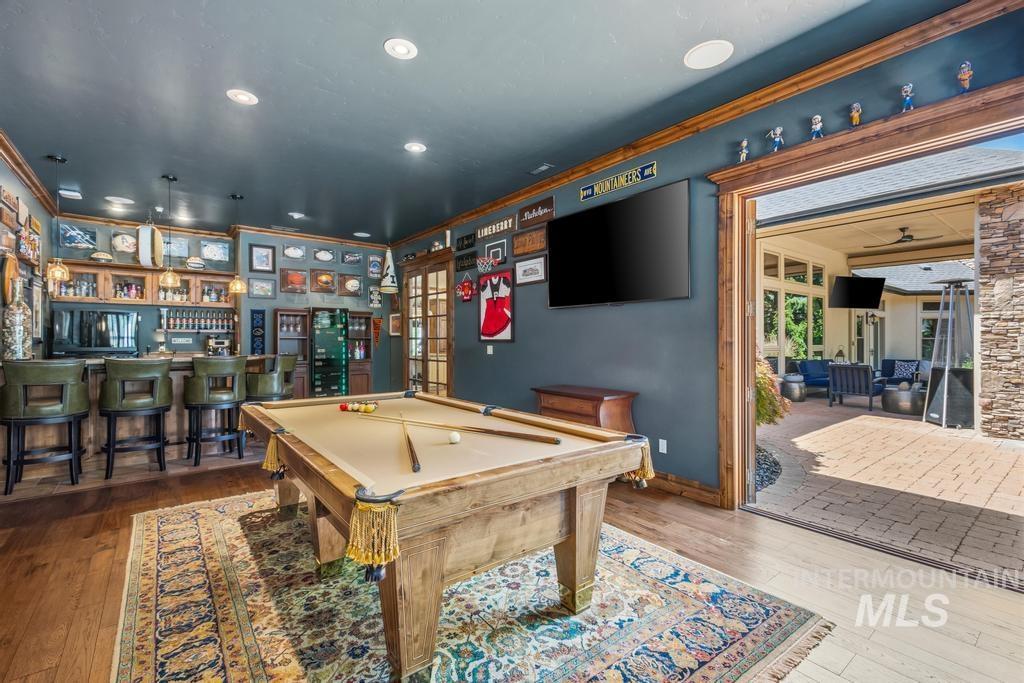 Spacious entertainment room featuring wood-finish flooring, a full-size pool table, and a built-in wet bar with overhead cabinetry