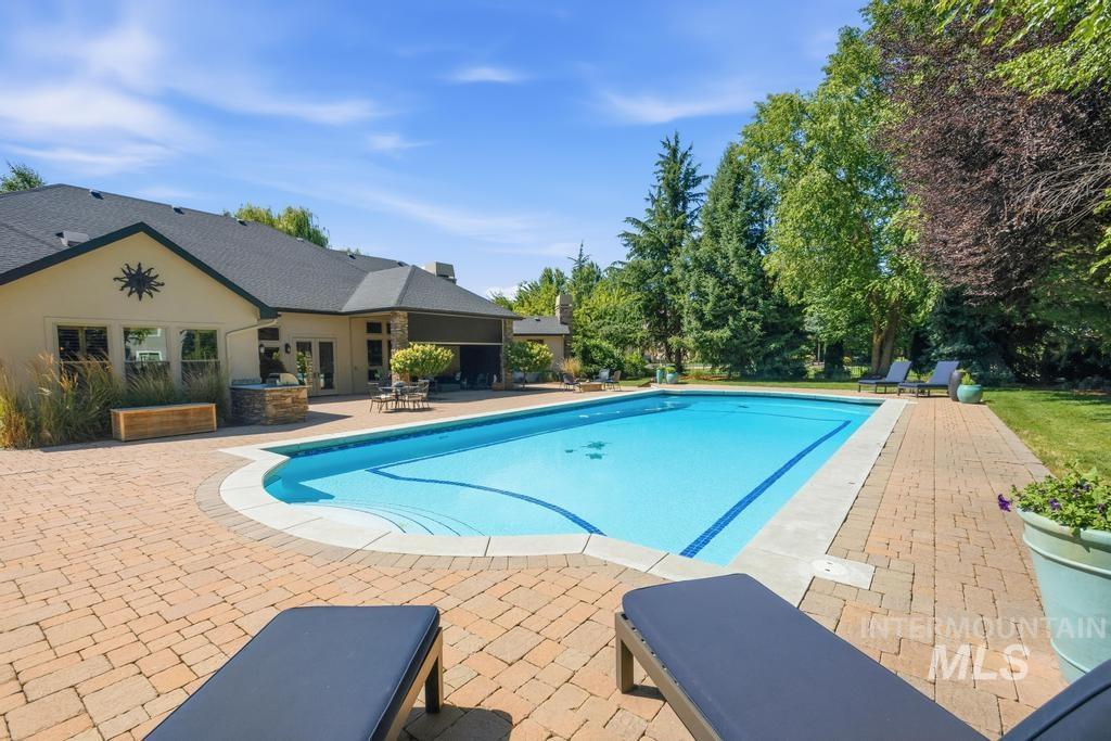 Outdoor swimming pool surrounded by a paver patio and mature landscaping