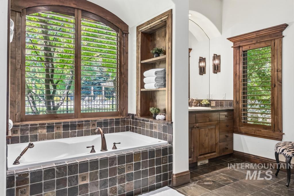 Soaking tub with bronze-finish fixtures set within a stone tile surround