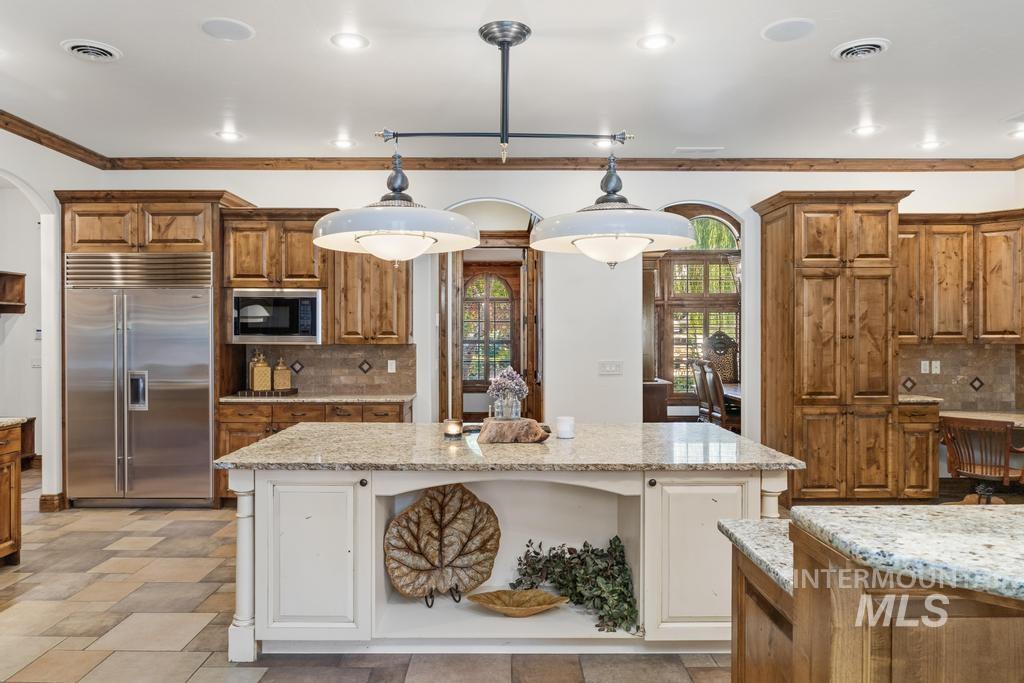 Spacious kitchen featuring a large central island with a light-toned countertop, rich wood cabinetry, stainless steel appliances, and tiled flooring