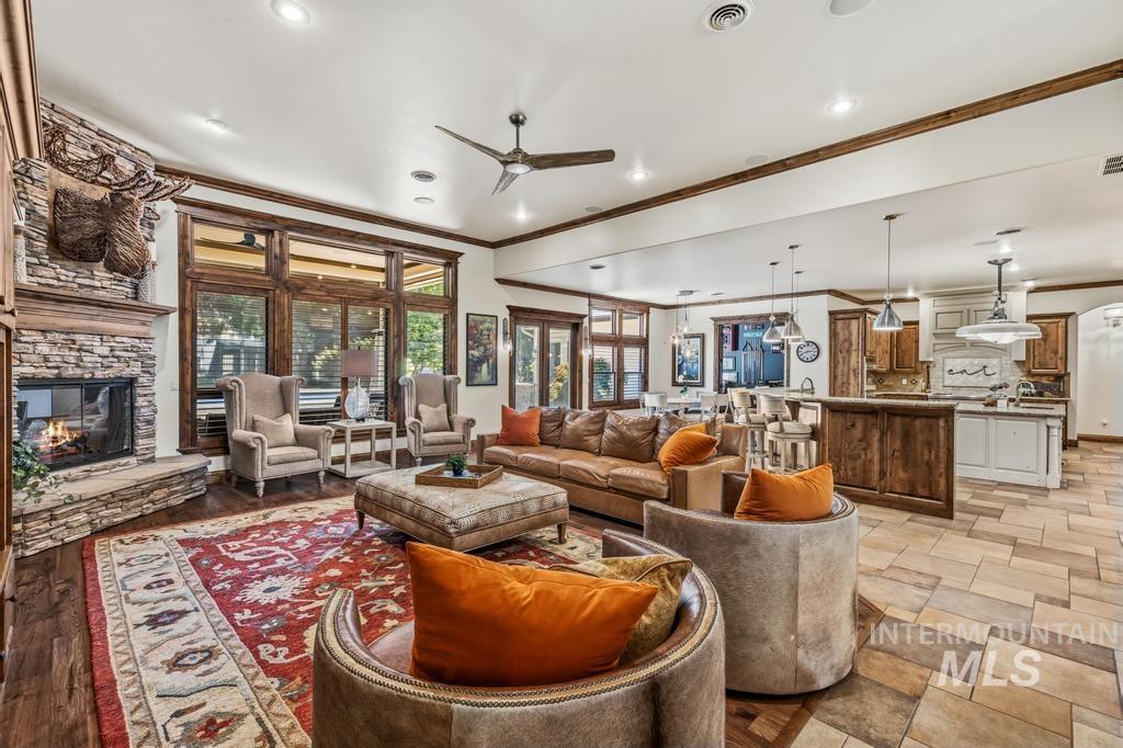 Spacious common area featuring a stone-clad fireplace with wood mantle, large windows with wood framing, recessed lighting, and a ceiling fan
