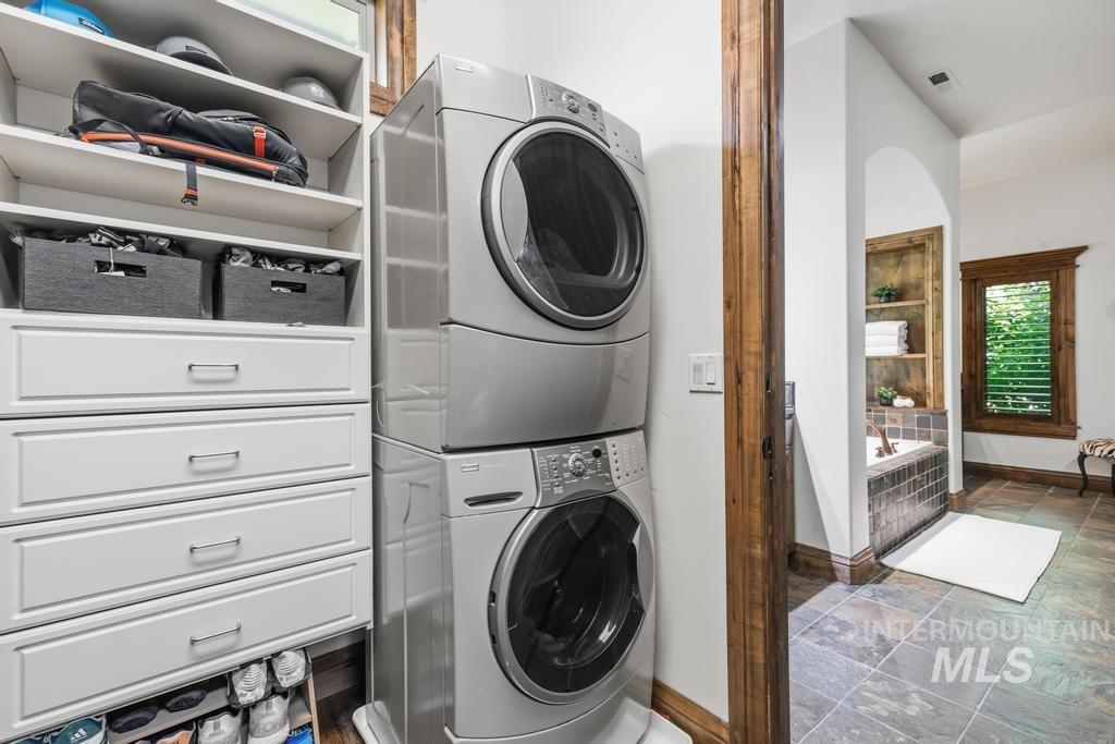 Integrated laundry area featuring a stacked washer and dryer, custom white cabinetry with drawers, open shelving, and a built-in shoe rack
