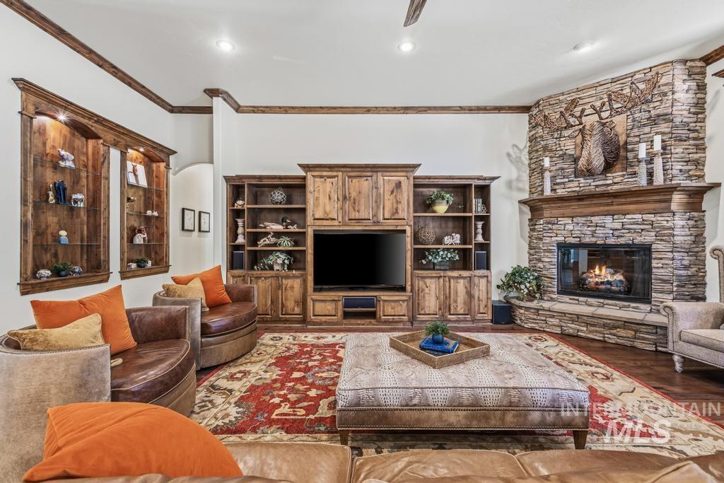 Corner stone fireplace with a wood mantel, built-in entertainment center, illuminated wall display shelving, wood-finish flooring, and crown molding