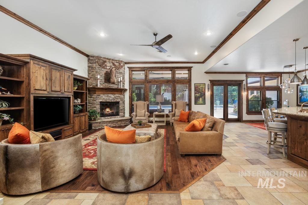 Spacious living area featuring a corner stone-clad fireplace, integrated wood cabinetry, a ceiling fan, and extensive windows with wood framing