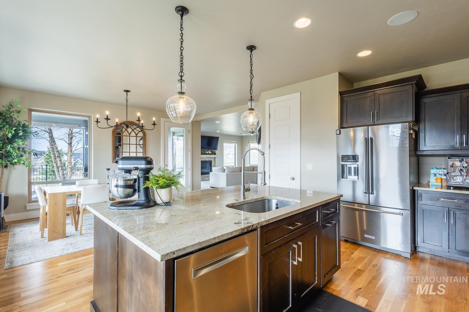 Kitchen with stainless steel appliances, light stone countertops, a glass covered fireplace, a center island with sink, and light wood-type flooring